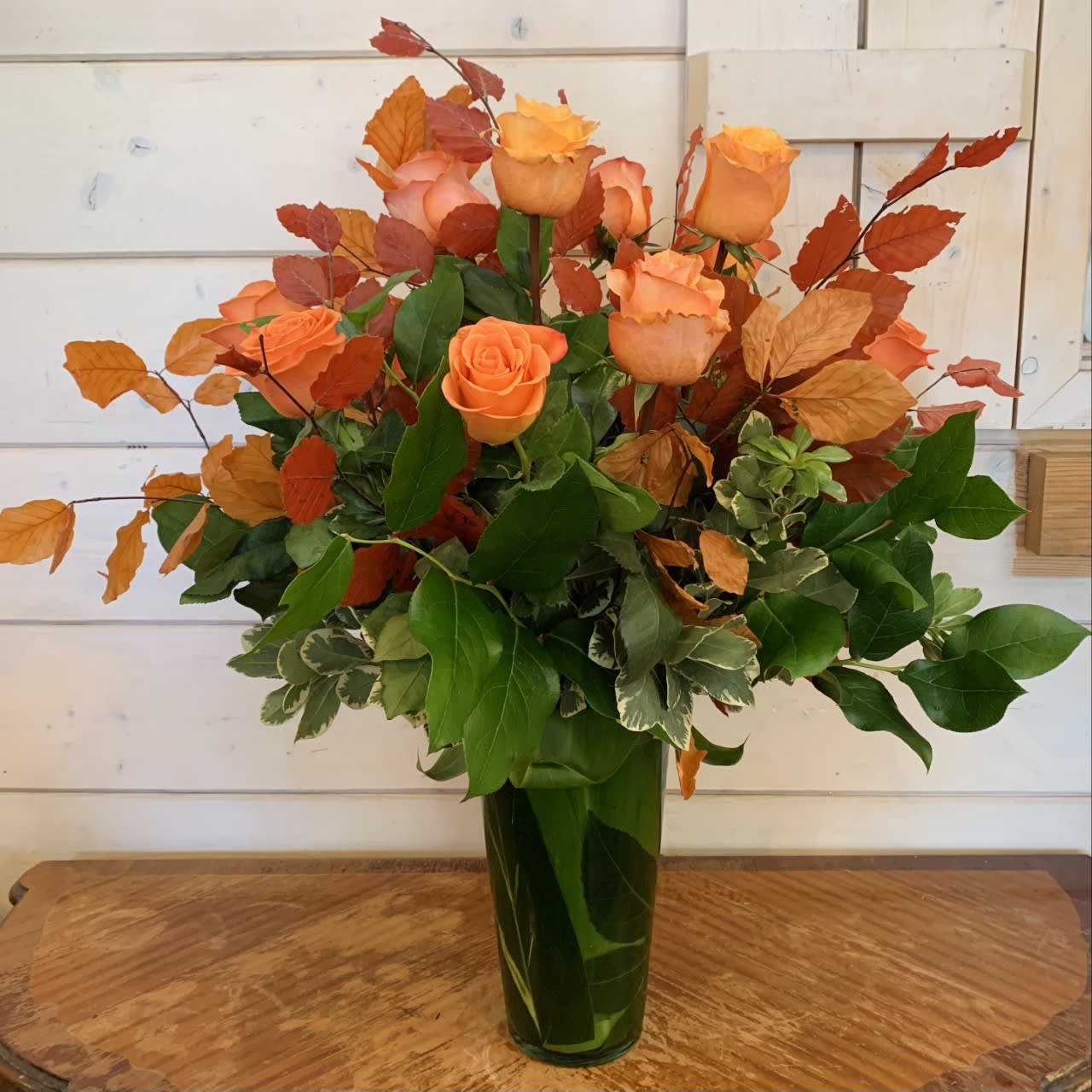 Autumn Rose Bouquet Autumn Rose Bouquet - A dozen long stem roses in a mix or oranges and apricots with seasonal fall foliage. Deluxe has 18 roses. Premium has 24 roses.