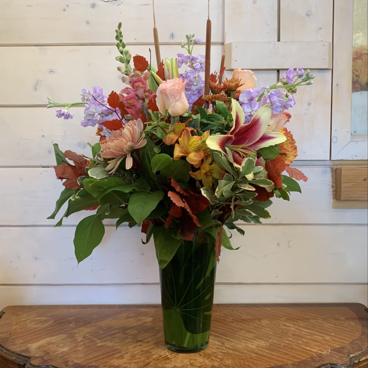 Fall Blessings  - Pale apricot roses, shocking lilies, orange snapdragons, lavender stock, orange alstroemeria, fall chrysanthemums arranged in a leaf lined French vase with copper beech and cat tails. Standard version is approximately 24in tall and 20in wide. 