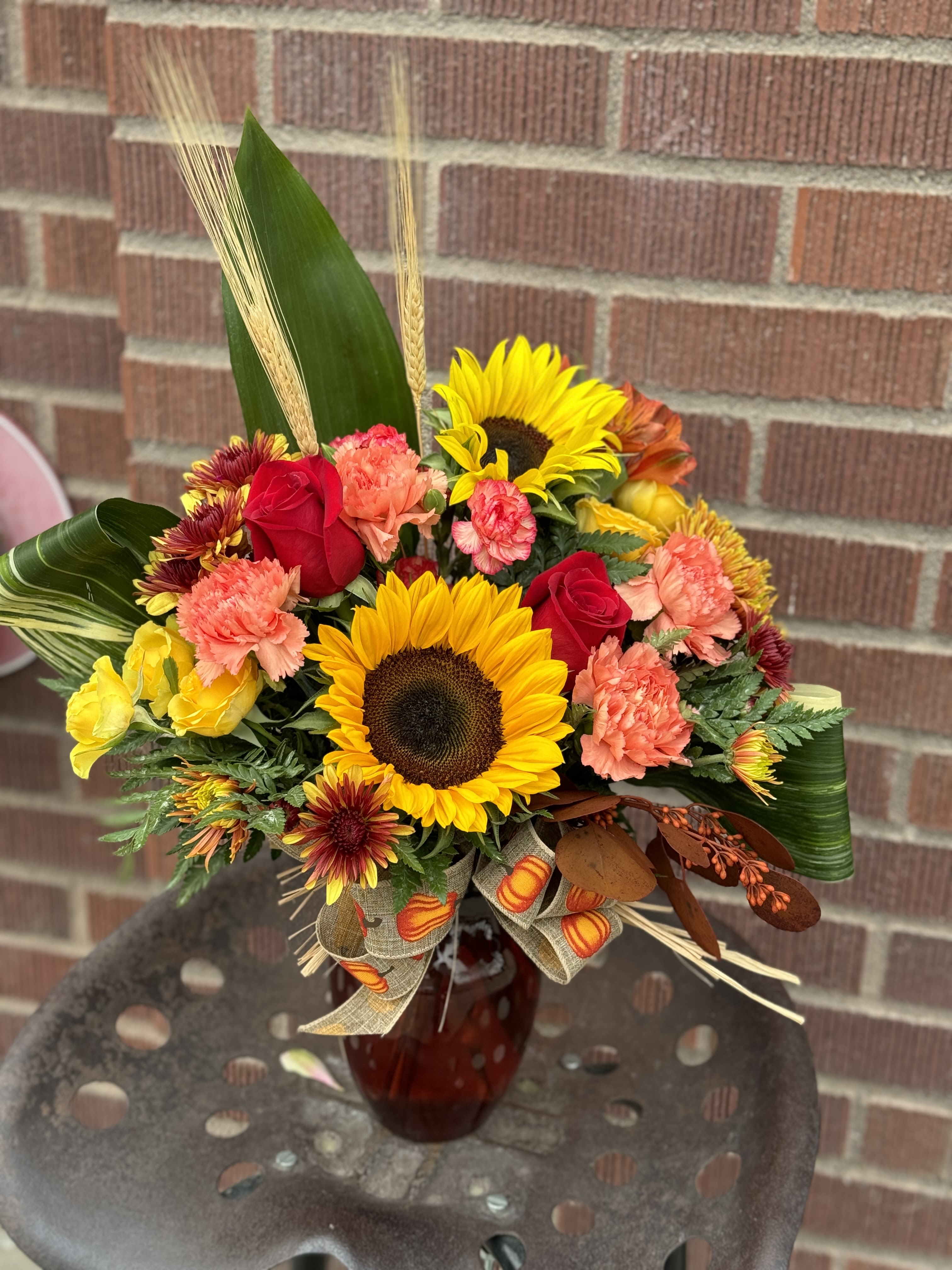 Flurry of Fall - Designed by one of our local gals, this arrangement contians sunflowers (in the rare instance we are out, we may sub with yellow gerberas), roses, rafia, carnations, and chrysanthemums in fall tones with a pop of white, invoking a fall feel with a touch of class. :) (Color of 8&quot; vase may vary)