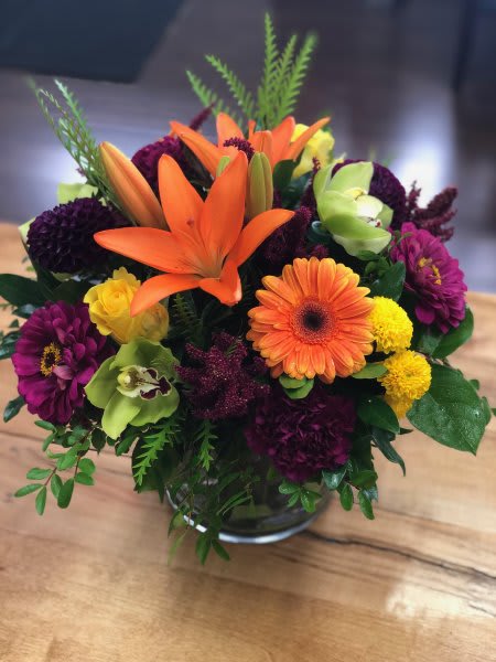 Autumn Sky Design Autumn Sky Design - A striking mix of orange lilies, golden gerberas, rich burgundy blooms, and vibrant green orchids—this lively arrangement captures the energy of the season. Designed in a clear glass vase with lush greenery, it’s perfect for celebrations, fall décor, or sending a burst of cheer.
