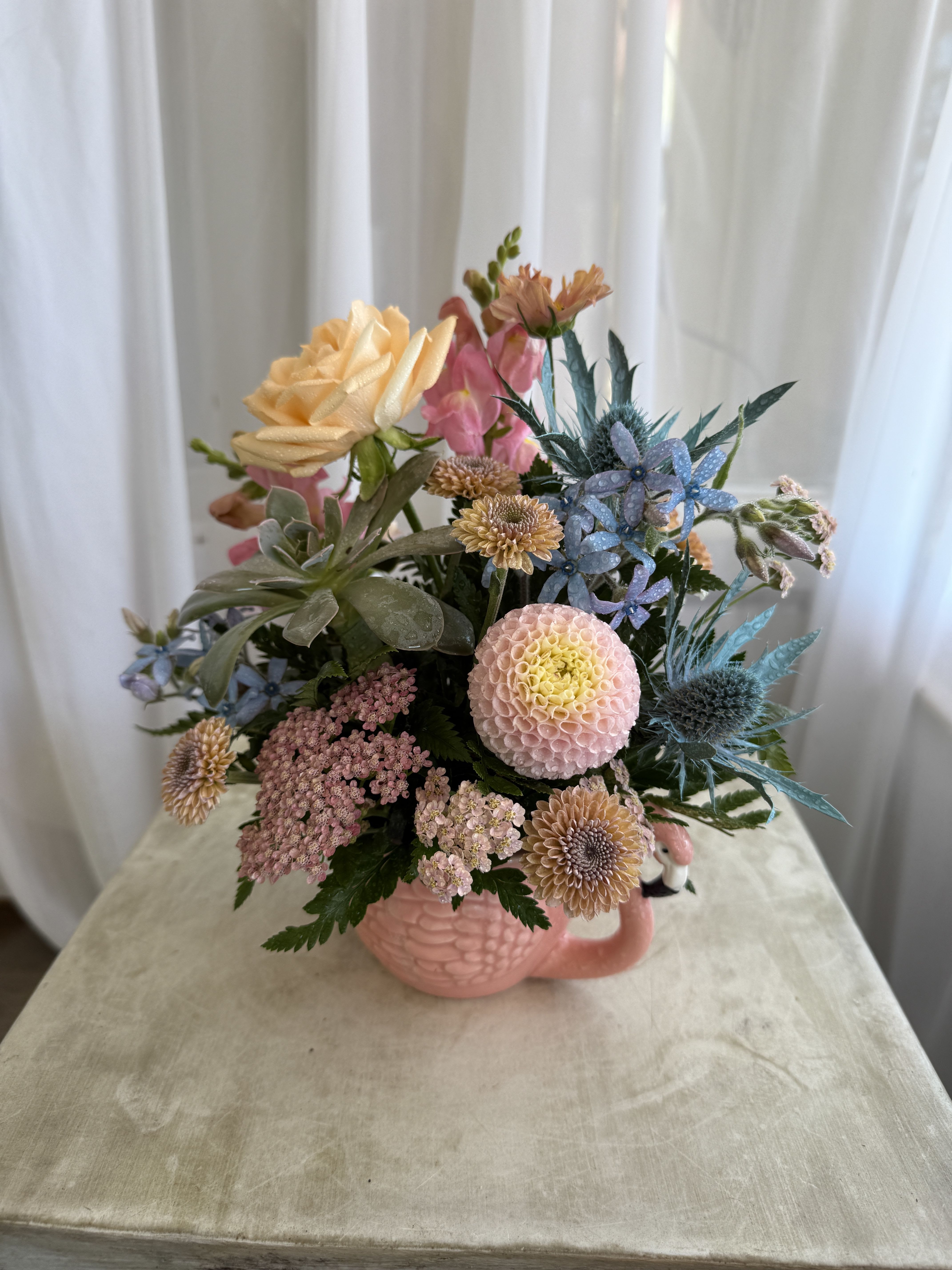 Flamingo Teacup Flamingo Teacup - This flamingo teacup arrangement could be the perfect arrangement for your mother, or another special someone in your life. The standard size features several sweet summer blossoms such as dahlias, chrysanthemums, and snapdragons. As always. this design is subject to substitution based on what is in stock.