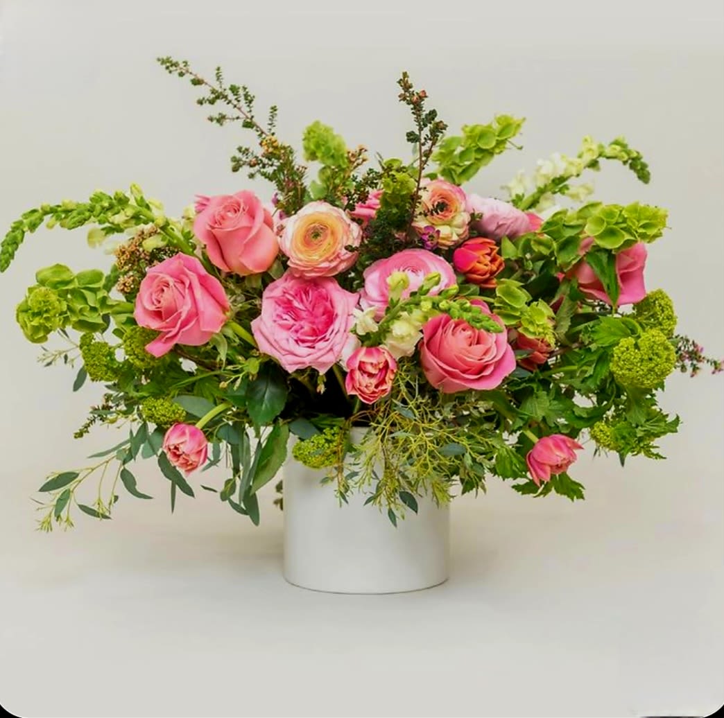 Floral Fancy by Pretty in Petals  - The bouquet is arranged in a white cylindrical vase, emphasizing a lush, rounded silhouette. The composition balances vertical elements with rounded blooms, creating a full and visually engaging display suitable for both decorative and formal settings.