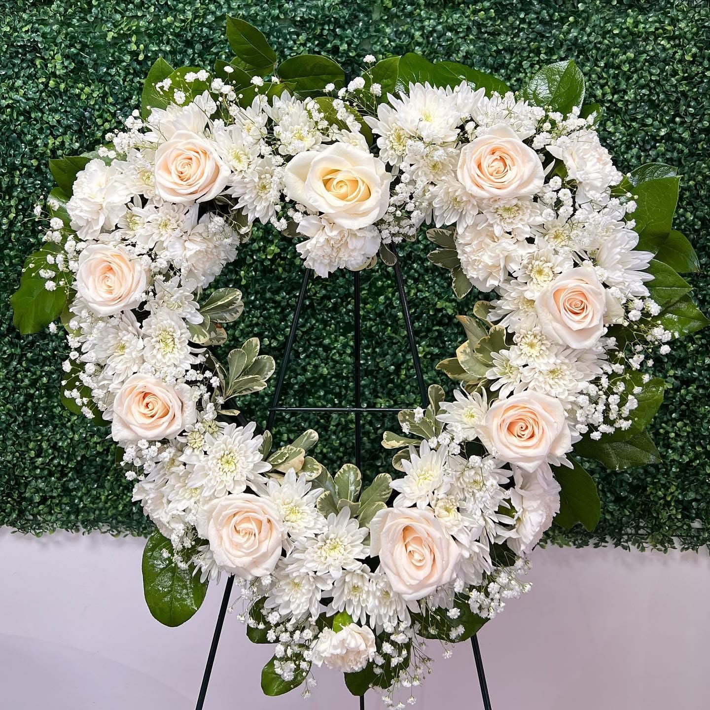All White Standing Heart - An elegant, all white, standing heart arrangement with roses, cushion mums, baby’s breath, carnations, and greenery. The blend of soft and delicate flowers creates a beautiful piece that can be gifted to loved ones that are grieving. Traditionally used as decorum for funeral services. Measures approximately 23 inches height x 24 width. Easel is included. 