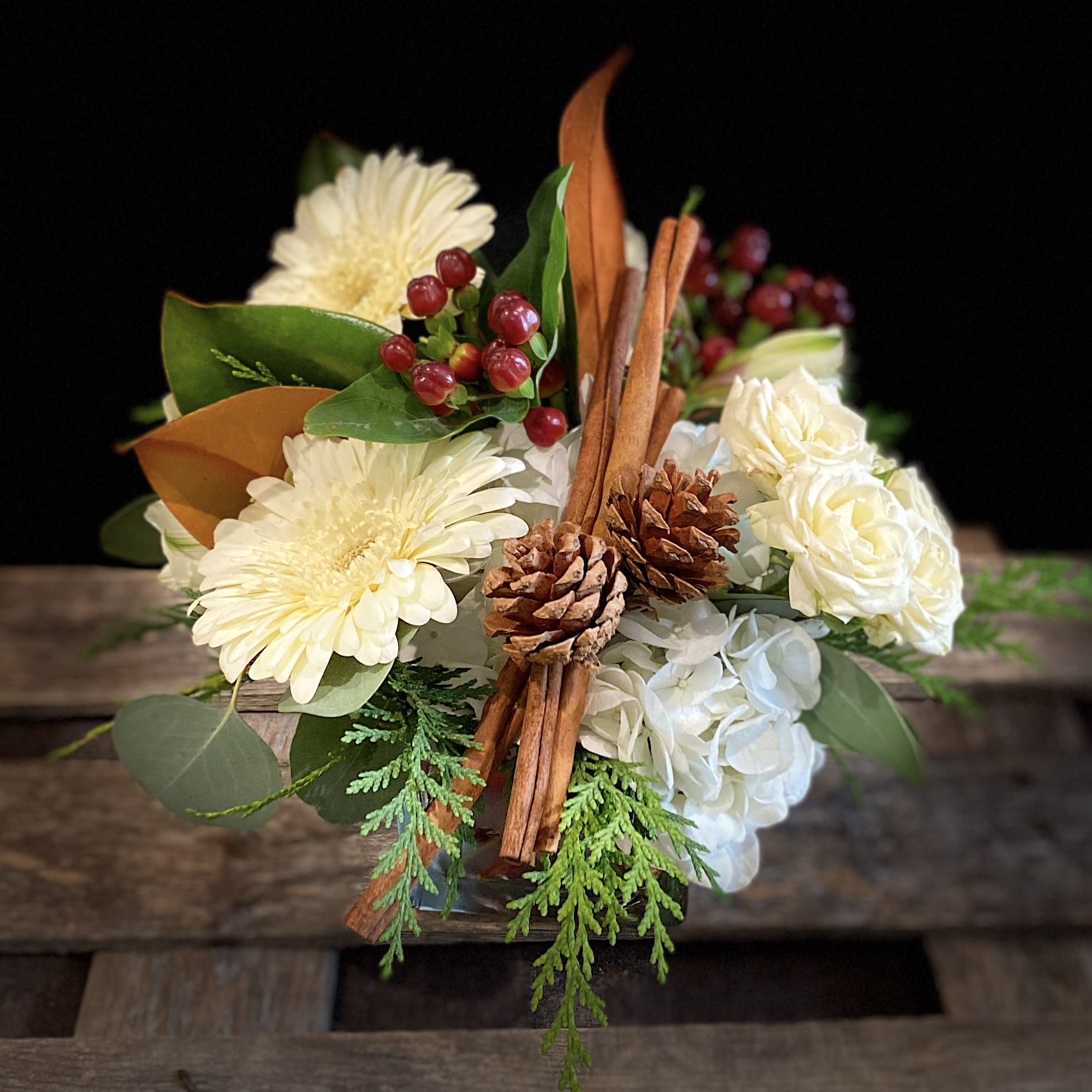 Cinnamon Sugar - A sweet, low centerpiece, filled with winter greens, lush hydrangea, spray roses, and alstroemeria accented with cinnamon sticks and pine cones. A holiday surprise that's certain to please!