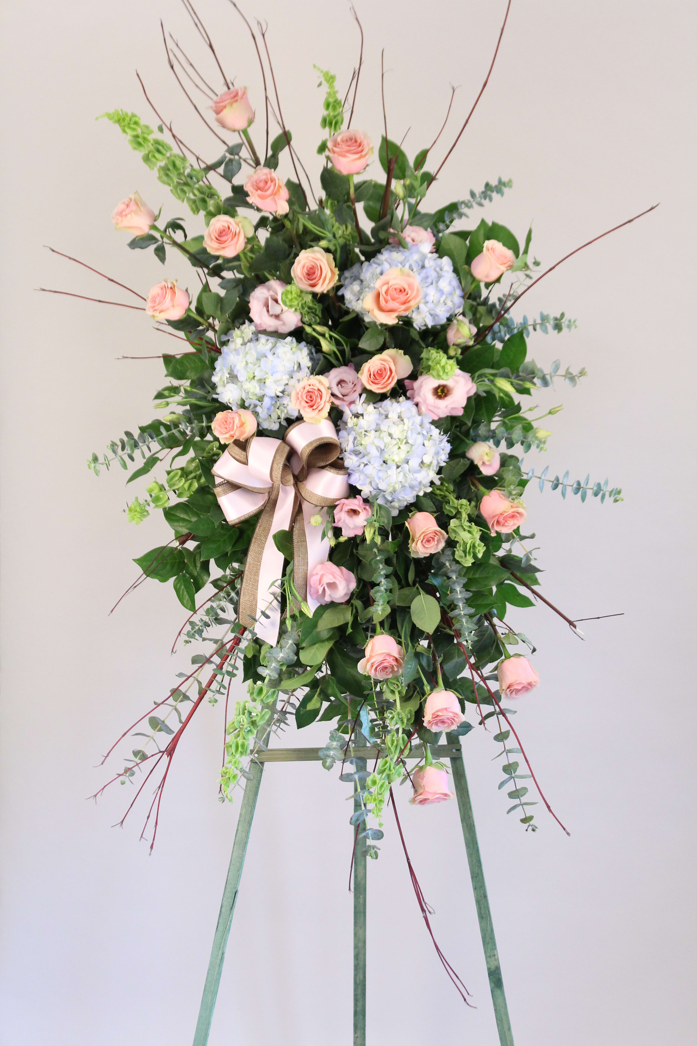 Heavenly Garden Spray Shades of Pink - Express deep condolences and strong hopes for the future with an elegant tribute that conveys admiration, affection, and respect.  Flowers may include roses, hydrangeas, lisianthus, bells of ireland, eucalyptus and branches.  Easel Stand Height: 5 1/2 ft.  Approx. Size: 6 ft. H x 24&quot; W