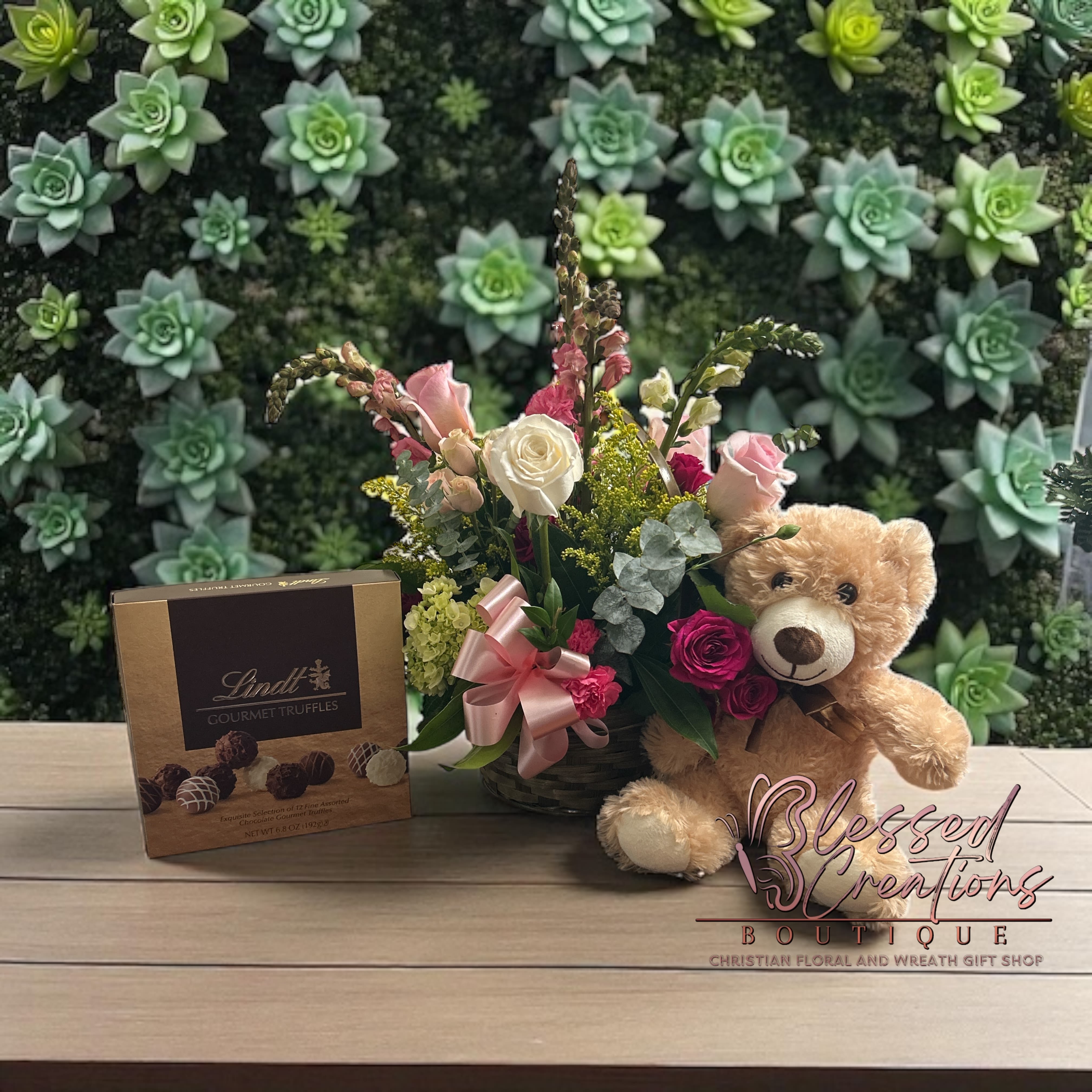 Sweet blessings gift basket  - A heartfelt gift filled with love and comfort. This charming basket features a beautiful blend of pink and white roses, carnations, hydrangeas, snapdragons, golden solidago, and lush greenery, all accented with a delicate pink bow. To make it even sweeter, it includes a cuddly plush teddy bear and a box of decadent Lindt gourmet truffles, creating the perfect gift for any occasion—birthdays, get well wishes, anniversaries, or simply to show someone you care.