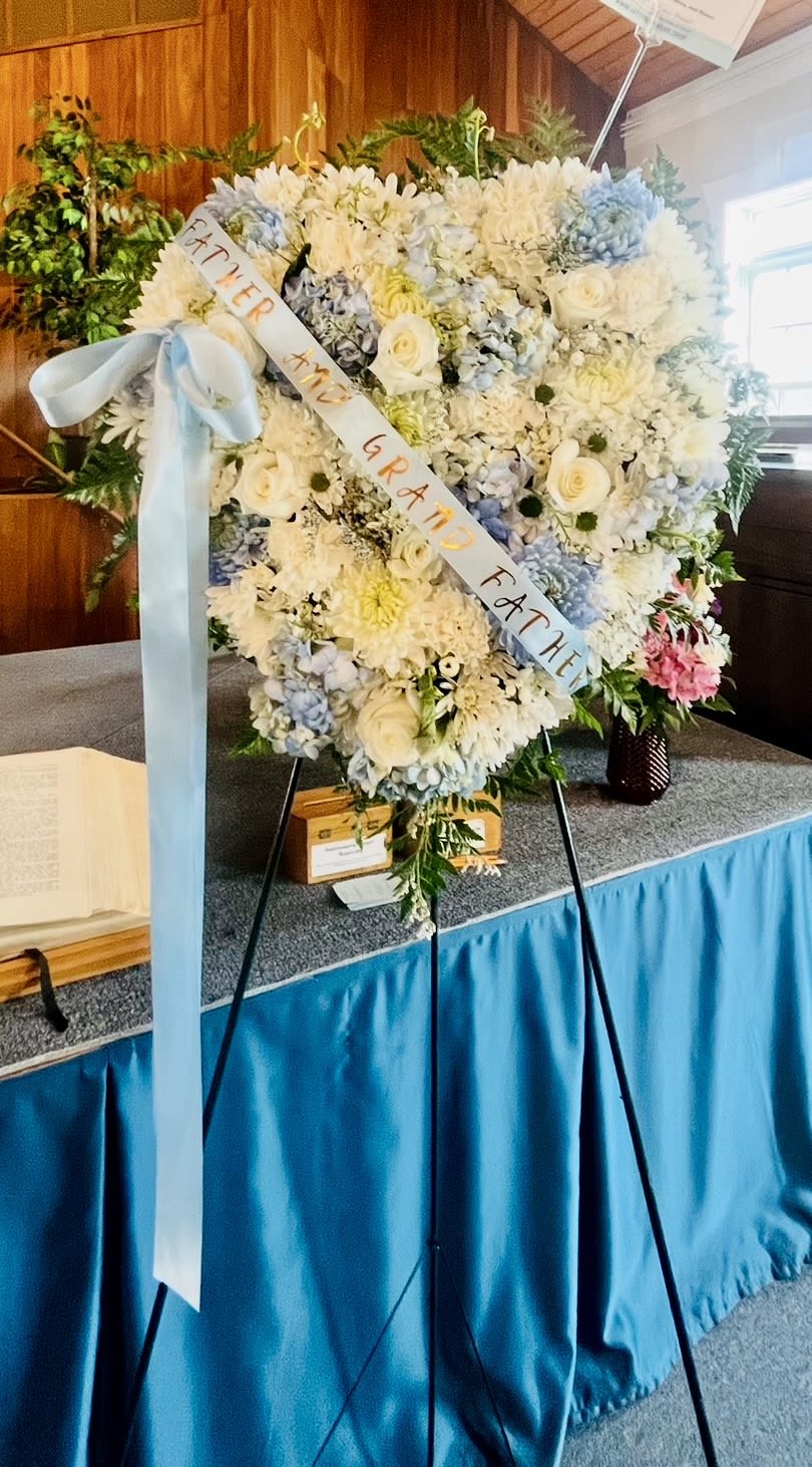 Heart-Shape Standing - White/Light Blue - White roses, chrysanthemum, carnations, Blue hydrangea and leather leaf greens. Sky blue ribbon.  Size: 18” 1/3 inches approximately 22” 1/3 inches approximately 24” 1/3 inches approximately 5 Ft. tall Stand (metal easel) Banner included.