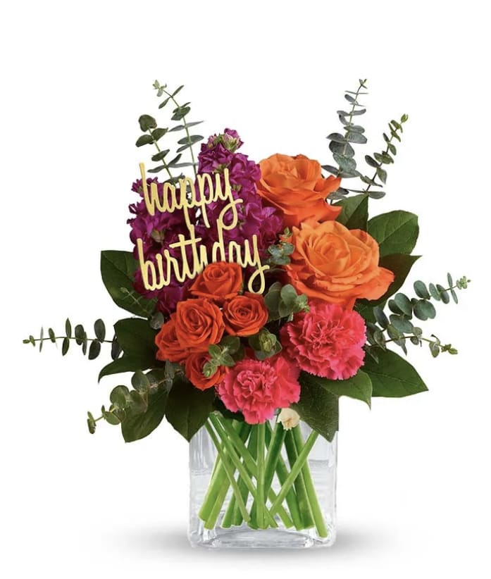 Radiant Arrangement - Orange and Hot Pink roses, Purple Stock, Hot pink Carnations, Eucalyptus, Lemon leaf, Clear Square vase, and Happy Birthday sign.