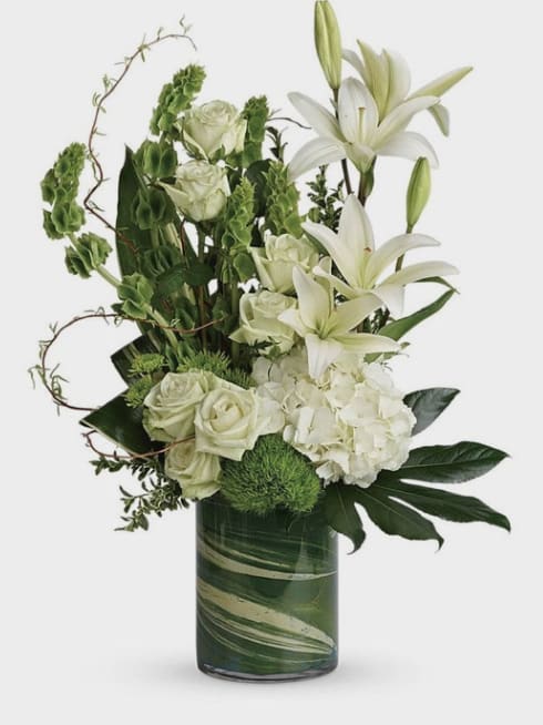 Green and White Elegant Arrangement - Green bells of Ireland, Dianthus, Aspidistra, White Lilies, Roses, Hydrangea, Bupleurum, Seasonal greens, in Clear Cylinder Vase.