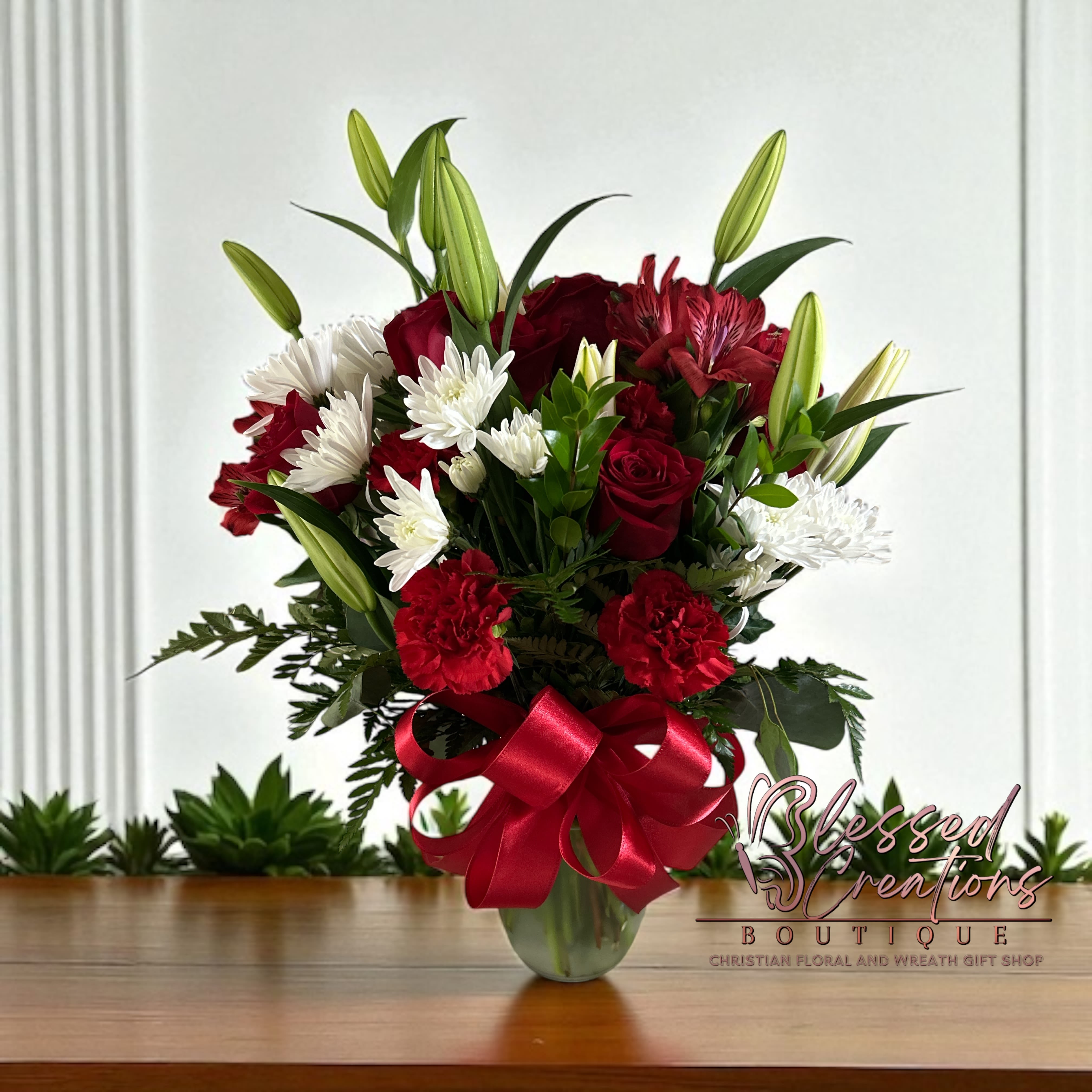 Forever in my Heart bouquet  - A bold and heartfelt expression of love and admiration. This radiant vase arrangement features classic red roses, vibrant red carnations, lilies, white mums, and lush greenery, all tied together with a rich red satin bow. Perfect for anniversaries, romantic gestures, or honoring a loved one with timeless elegance. 