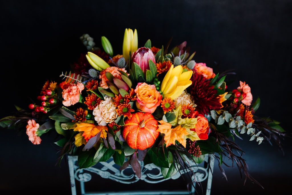 Autumn Orchard - Bring the richness of the harvest season to your table with Autumn Orchard. Bursting with golden lilies, burnt orange mums, soft carnations, protea, and vibrant fall leaves, this lush centerpiece is crowned with mini pumpkins and berries for a festive, orchard-fresh feel. A perfect choice for Thanksgiving gatherings or cozy fall décor.