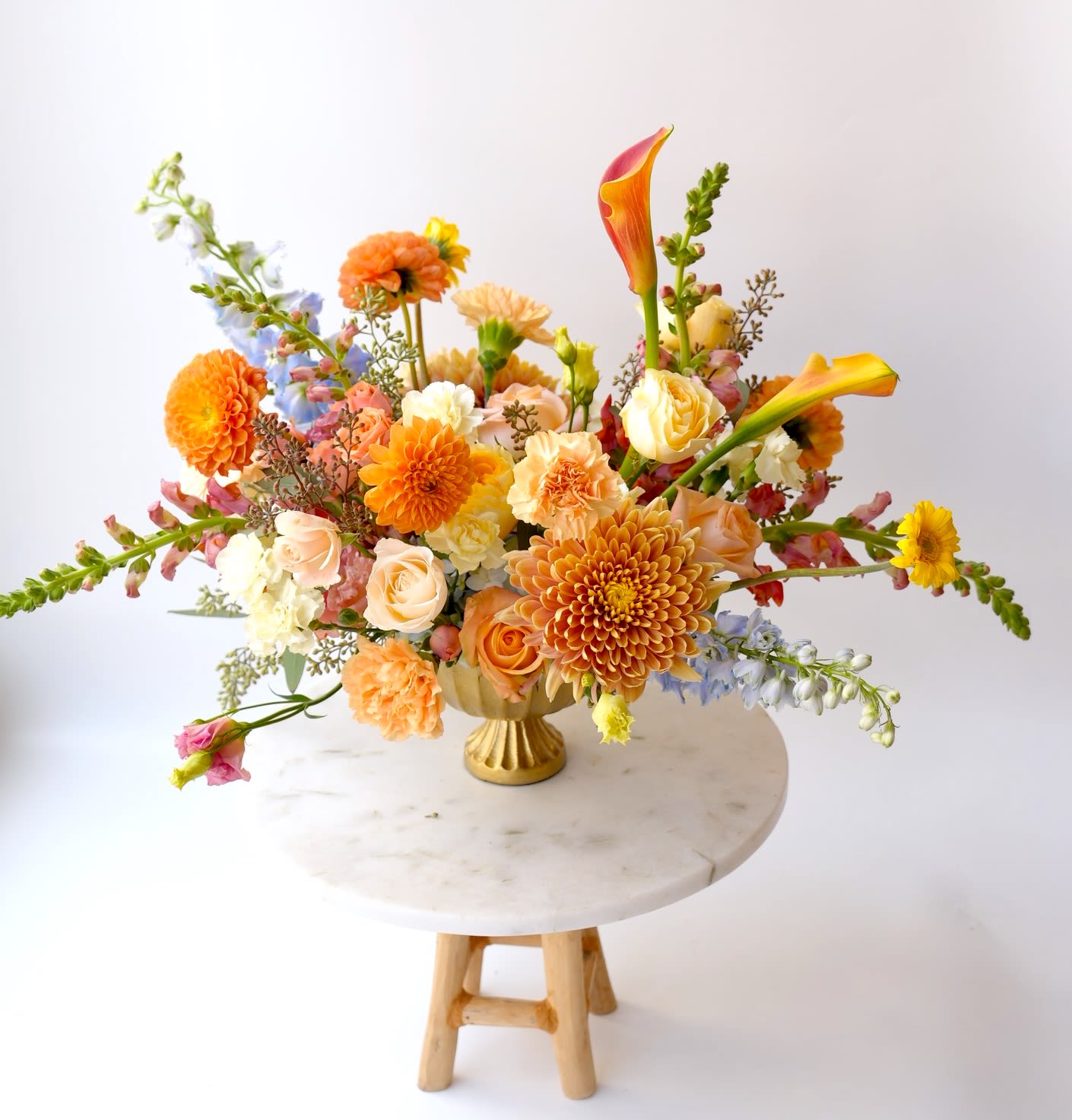 Autumn Bliss - The perfect blend of whimsy and tradition with this enchanting table arrangement. Warm oranges, soft peaches and sublte blue accents create a captivating centerpiece that complement anyholiday decor. Includes: roses, mums, delphinium, calla lilies and seasonal fillers.  Note: the actual product may slightly differ from the photo but we it will be made with the freshest flowers available. The vase is included.