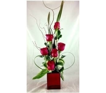 Lady In Red - A fantastic design of six red roses in a red cube with varrigated leaves, lily grass, and curly willow. A sure show stopper!