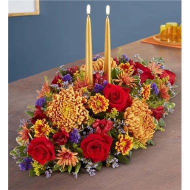 Brilliant Autumn Centerpiece - Set the table in brilliant style. Our new centerpiece captures the rich beauty of autumn in every last detail. Pops of red and bronze mix with lush greens. A gold tapered candle stands at the center, creating a warm and cozy ambiance for every gathering. All-around centerpiece arrangement with red roses and Peruvian lilies (alstroemeria), purple Limonium, bronze football mums, dark bronze cushion mums, bronze &amp; two-tone daisy poms; accented with assorted greenery 