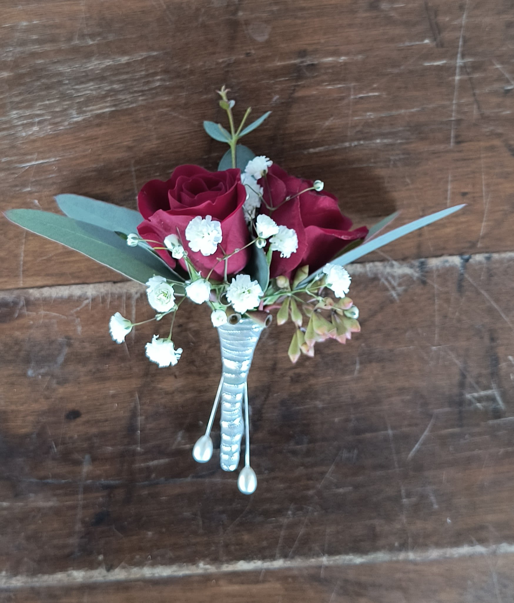 Rouge Boutonniere - Classic red roses fresh eucalyptus greens and baby's breath boutonniere with red spray roses accented with silver ribbon.
