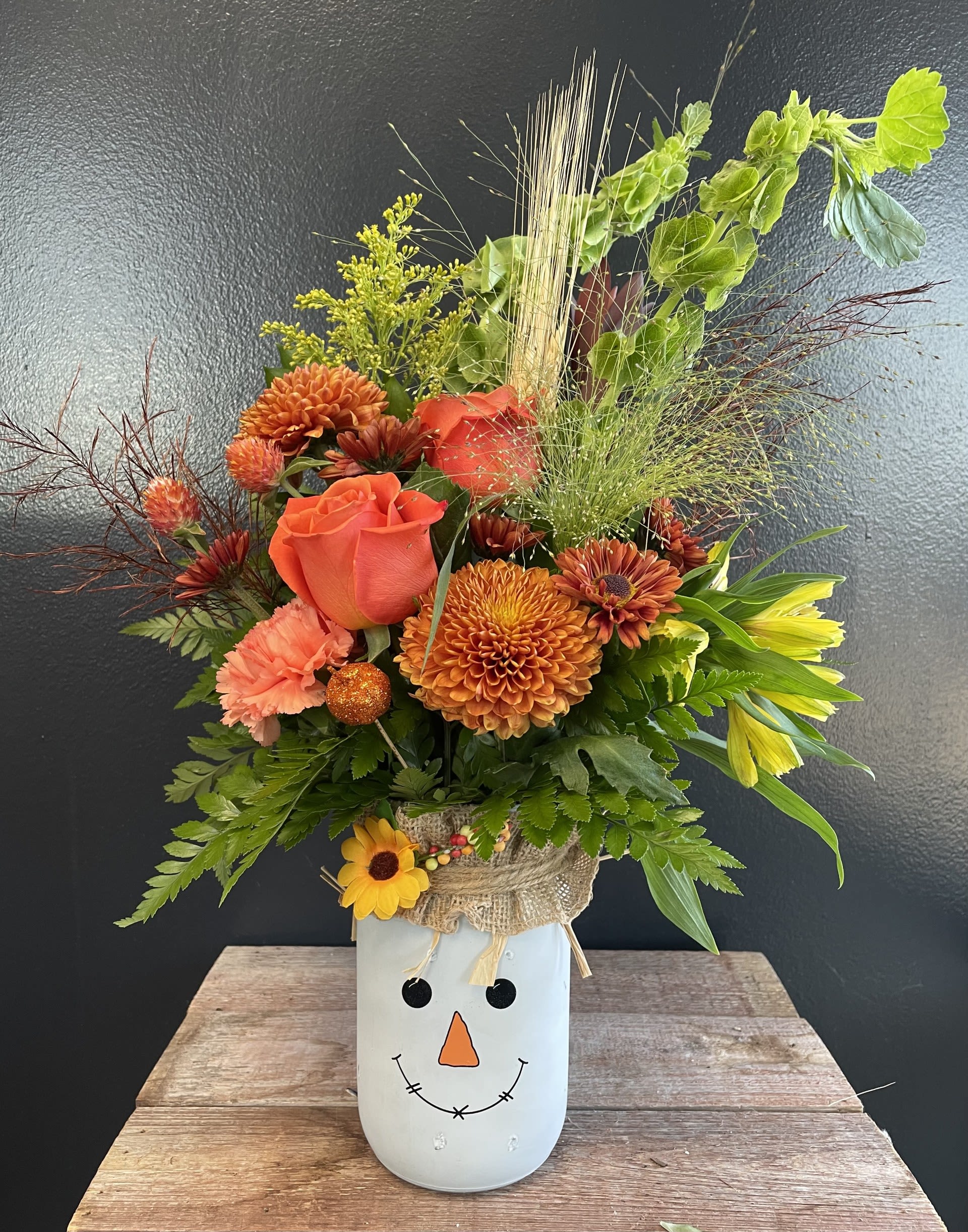 Scarecrow  - Celebrate the charm of fall with this delightful arrangement, designed in a whimsical scarecrow vase. This bouquet features a vibrant mix of autumn blooms.