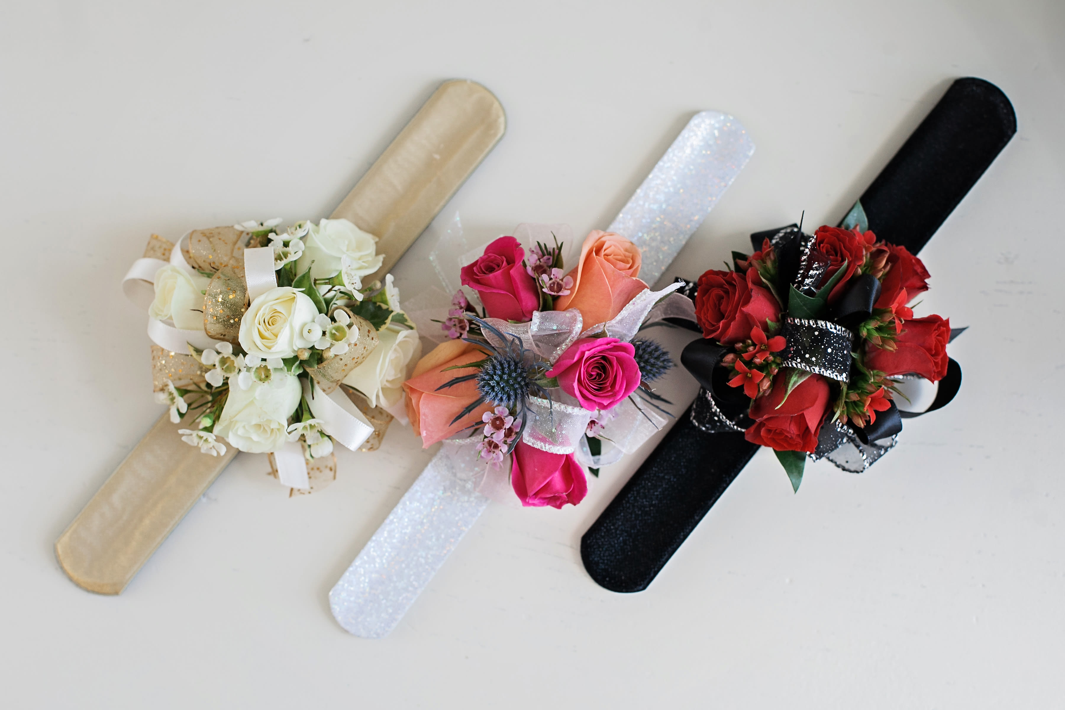 Spray rose corsage on a slap bracelet - Pick Up Only - The slap bracelet corsage features spray rose blooms, is accented by filler flowers such as waxflower or limonium, and is finished with foliage and ribbon. Tell us the dress color and we can suggest matching flowers, ribbon and bracelet bases. Bracelet colors - Silver, gold and black. Spray rose colors - white, red, pink, coral, purple, orange and yellow. Ribbon colors - we have a lot of colors available! 
