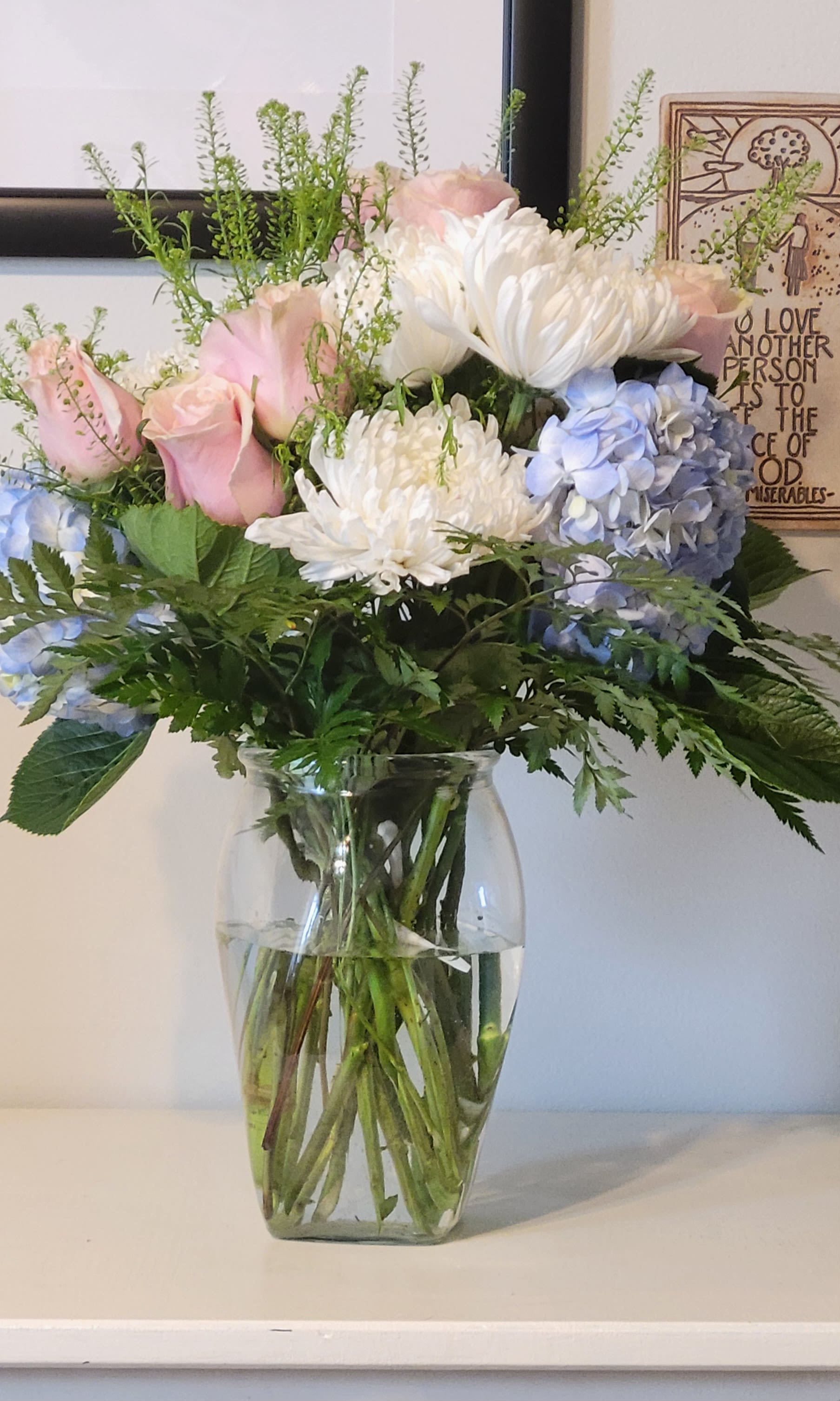 Breezy by the Sea by Dixie's Flowers Breezy by the Sea by Dixie's Flowers - “A soft, airy bouquet featuring pink roses, delicate white poms, complemented by wisps of delicate greenery. The arrangement has a light, romantic feel with a natural, garden-inspired style.”