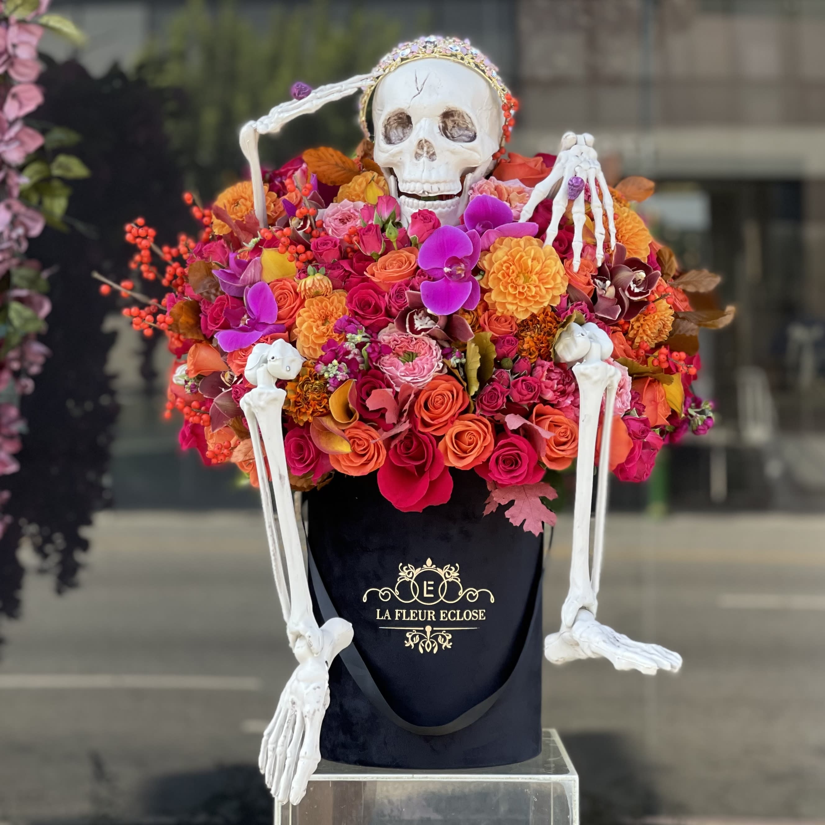Koko the Skeleton  - Orange and hot pink arrangement of fresh flowers in our signature black velvet box with a skeleton, wearing the shiny crown and a scull ring 