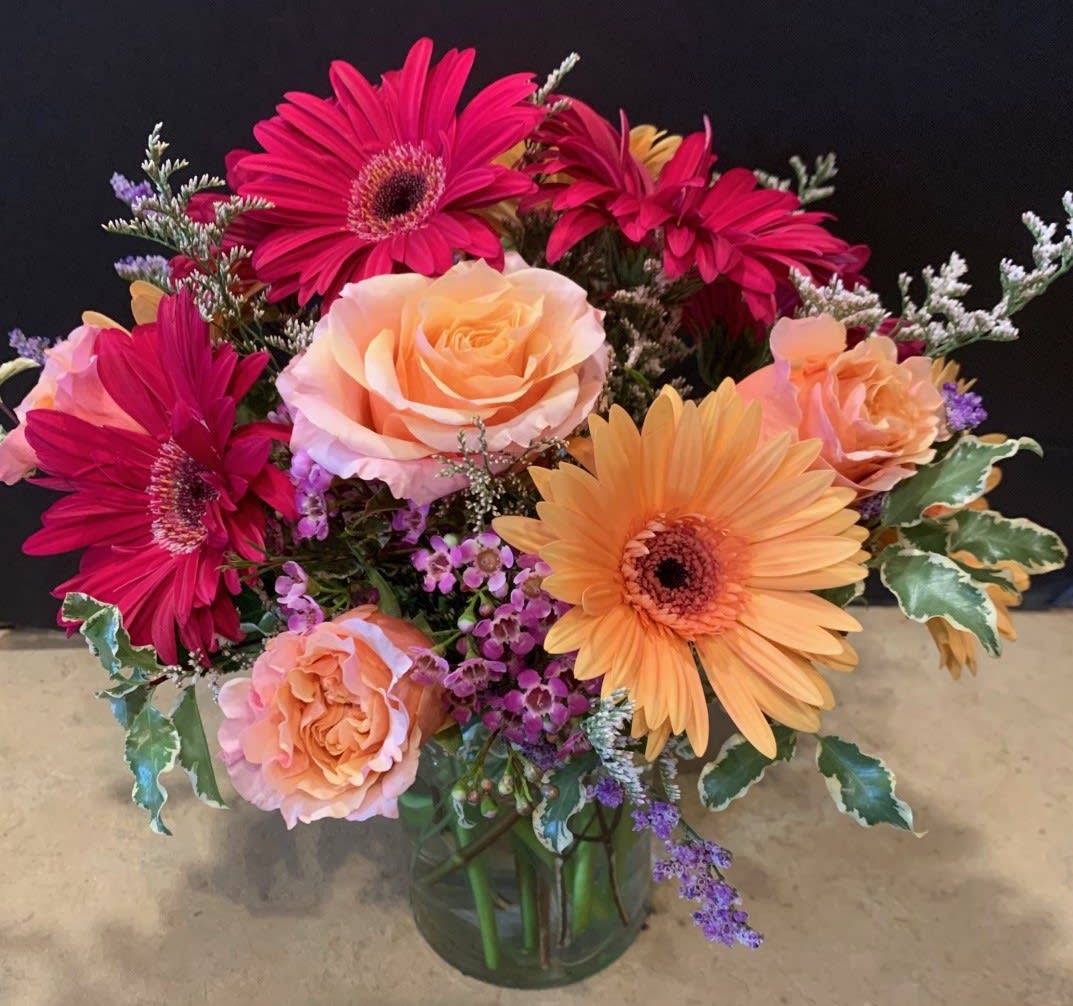 Mia's Bouquet   - This special arrangement of jewel tone Gerbera daisies and Roses will bring happy smiles.  Our upgrades will include additional fresh blooms. Designed in a pave, low and lush style.  