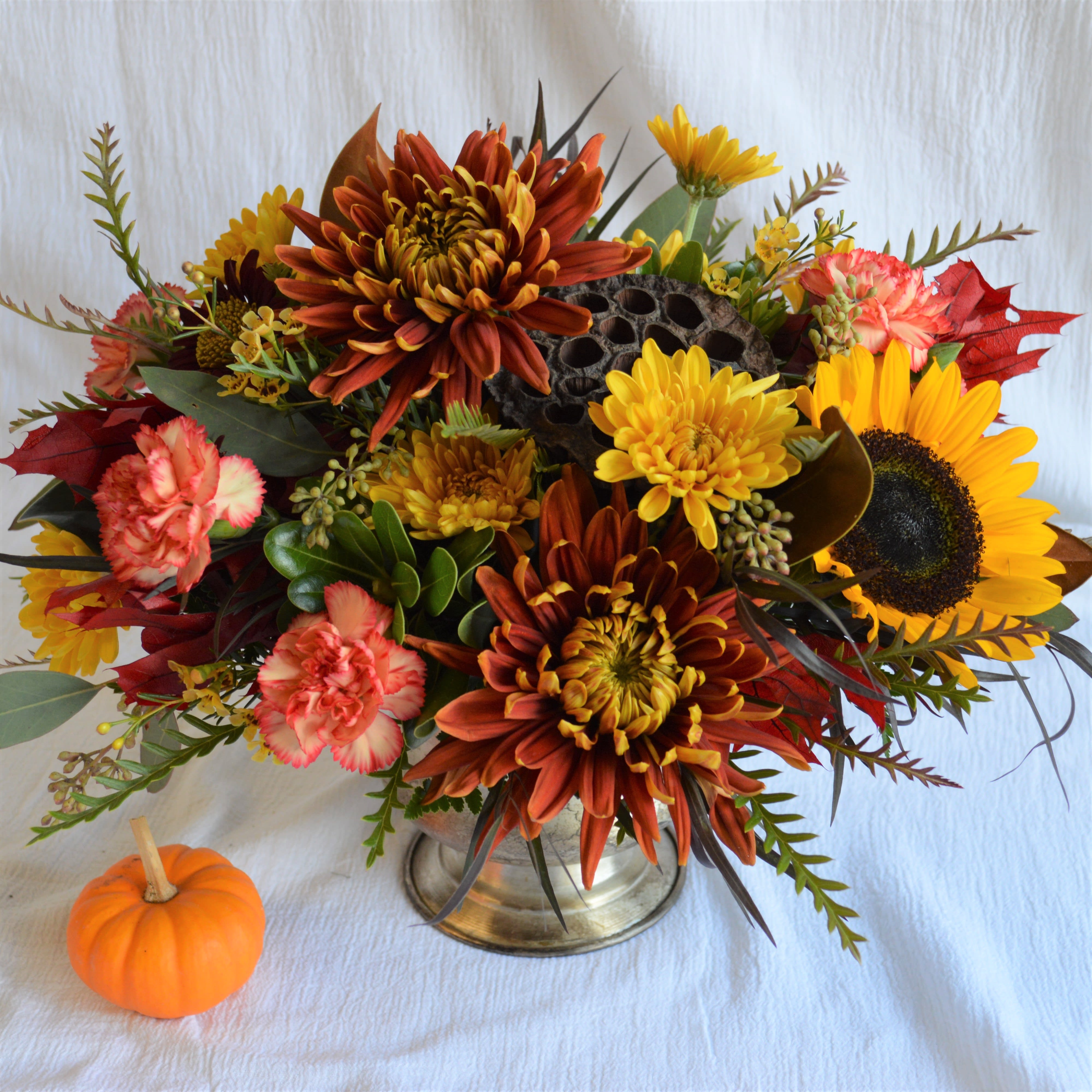 Nina - A brushed silver footed compote full of fall flowers in a warm color palette, and accented with autumn leaves. This fresh arrangement is perfect for your holiday table, or as a gift to the hostess. Approximately 13&quot; wide x 11&quot; tall.