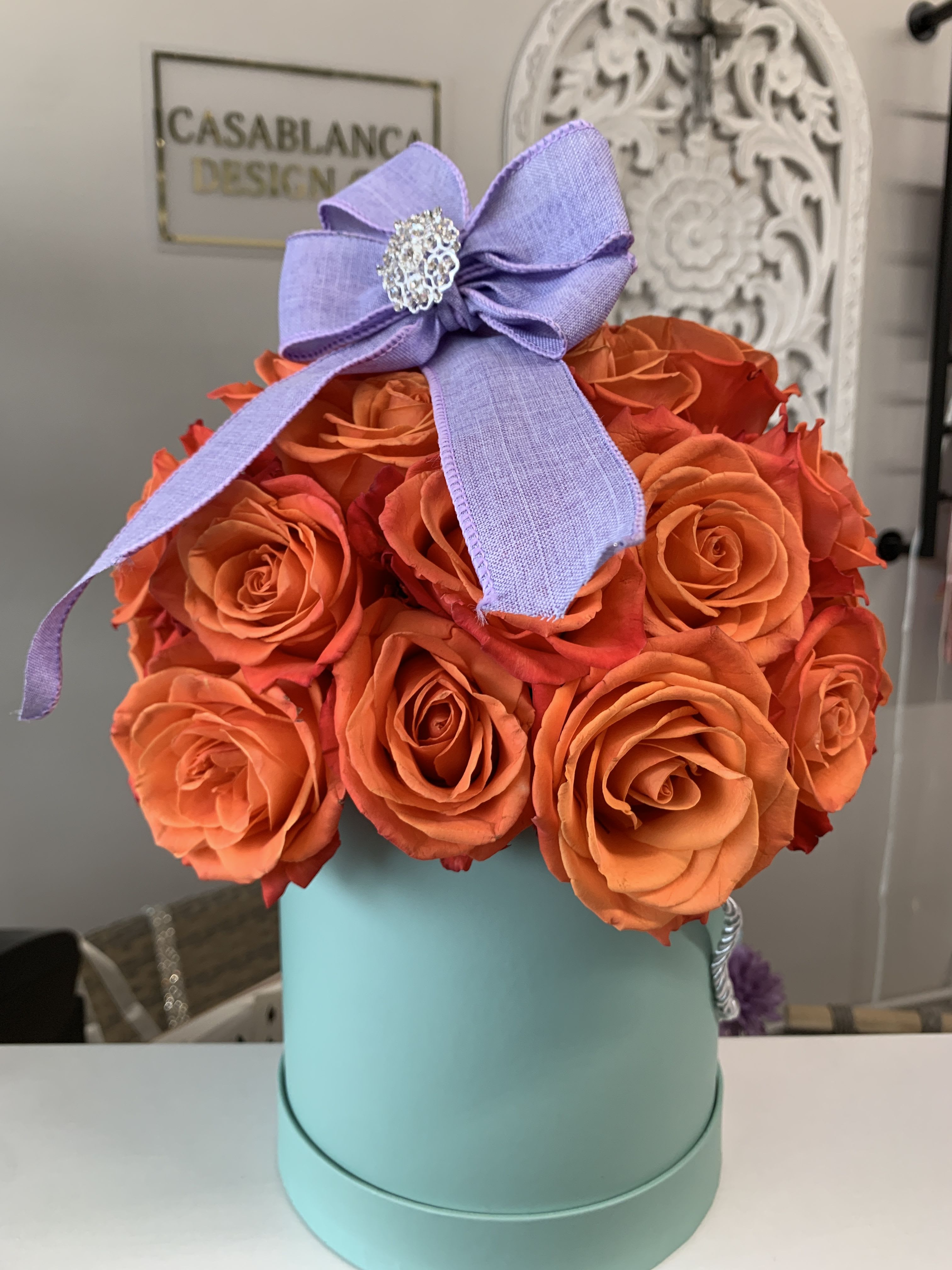 Ariel Ariel - Orange roses in a light teal box with a purple bow.