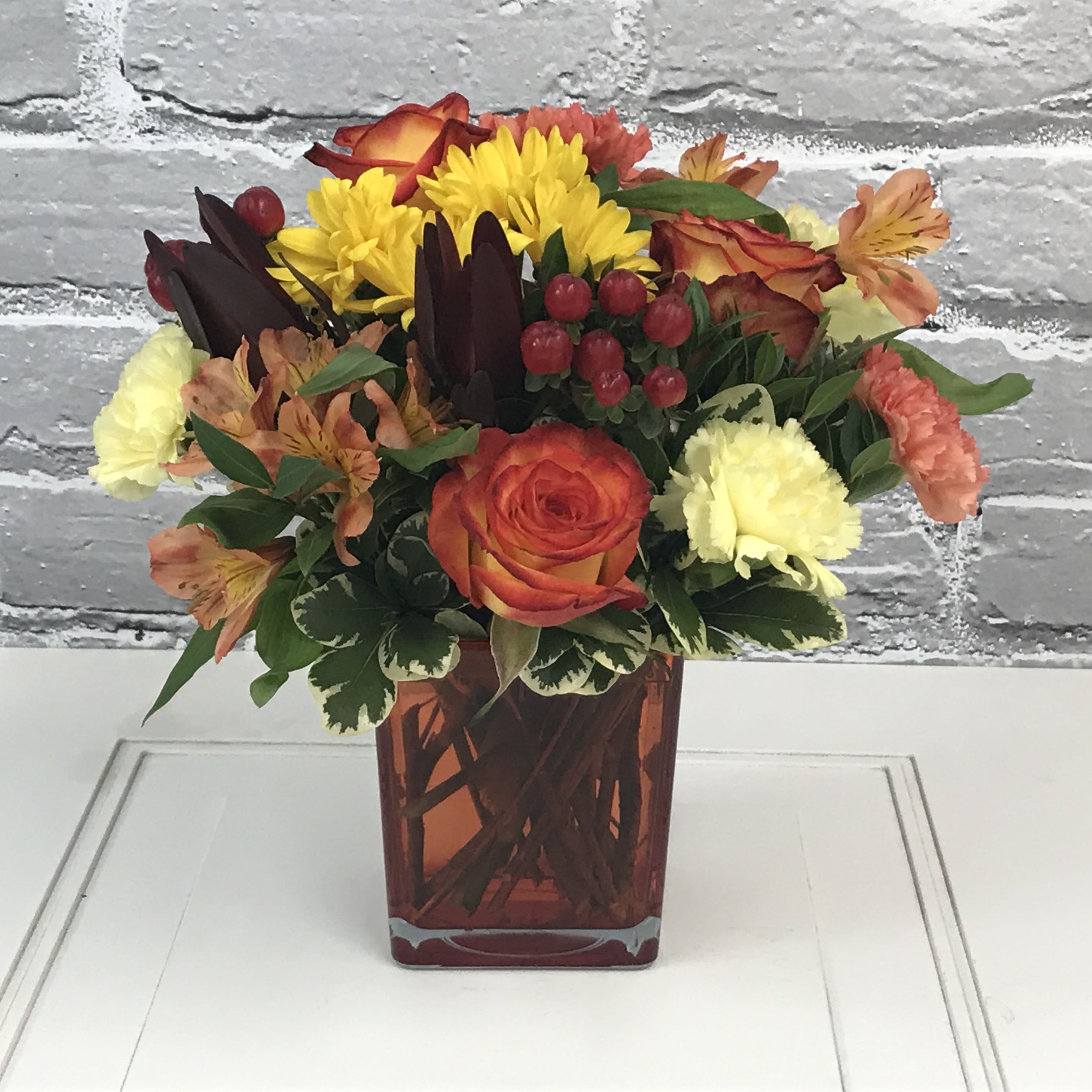Changing Seasons - Bright orange cube overflowing with bright autumn oranges and yellows. Roses, carnations, alstromerias, berries and lush greens fill up this beauty! **Flowers may vary from the picture, but the overall theme and style will remain! **