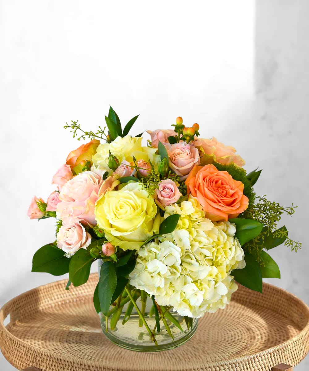Sunset Garden Sunset Garden - Bring the warmth of a golden-hour glow into your space with the Sunset Garden arrangement. Designed to evoke the soft, romantic colors of a setting sun, this stunning bouquet features a delicate blend of light pink, peachy-orange, and creamy white blooms. Nestled in a clear glass cylinder vase, the arrangement includes lush hydrangeas, elegant roses, dainty spray roses, and rich greenery for added texture and fullness perfect for any occasion. From heartfelt celebrations to everyday beauty, this fresh and modern design adds a graceful touch to any room. What’s included? A mix of Light Pink, Orange/Peach, and White Roses, Hydrangeas, Spray Roses, and Seasonal Greenery in a Clear Glass Cylinder Vase.