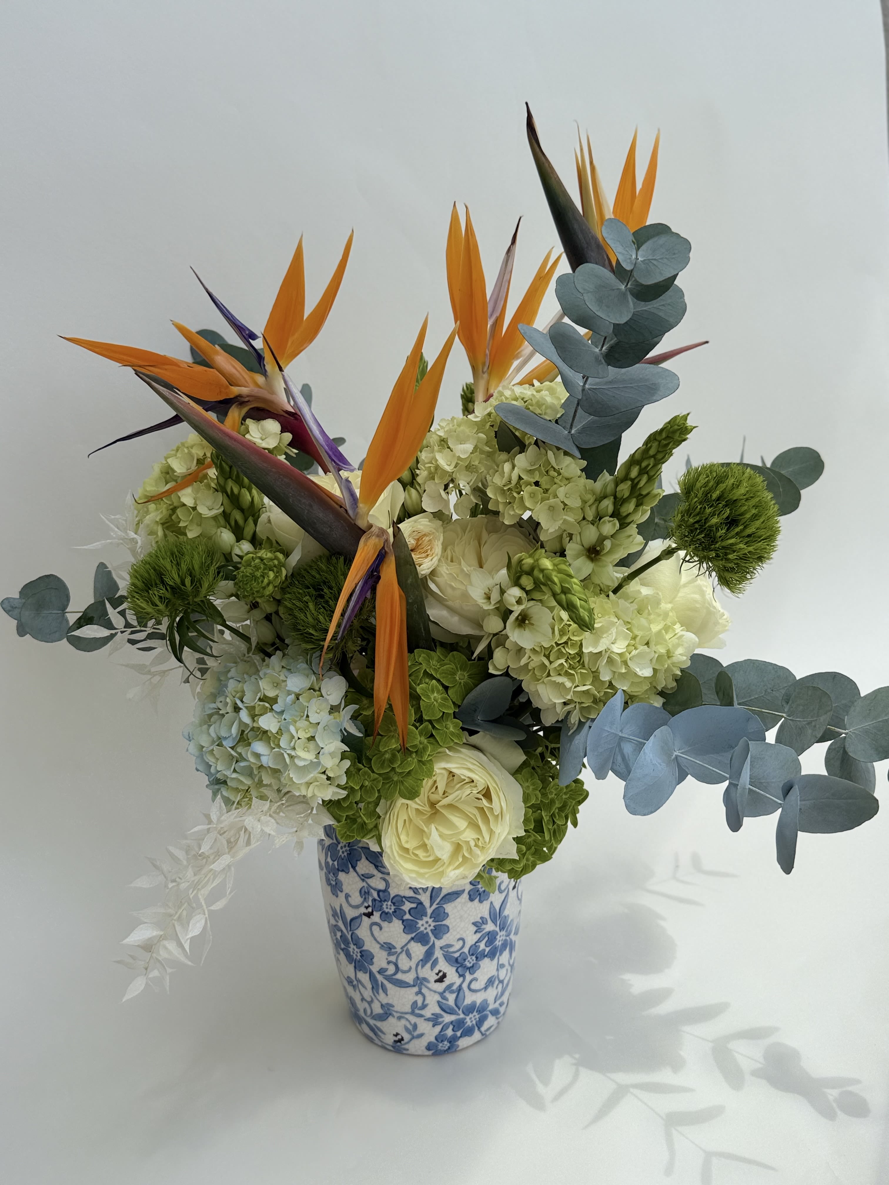 Paradise Bloom - Tropical-inspired arrangement brings together the exotic beauty of Birds of Paradise with soft elegance of hydrangeas. Fresh, modern, and graceful—crafted with care at Casa di Fiori. Flower Type: Birds of Paradise, hydrangeas, white garden roses, eucalyptus, green dianthus, ornithogalum.  The flower arrangement comes with a complementary vase. 