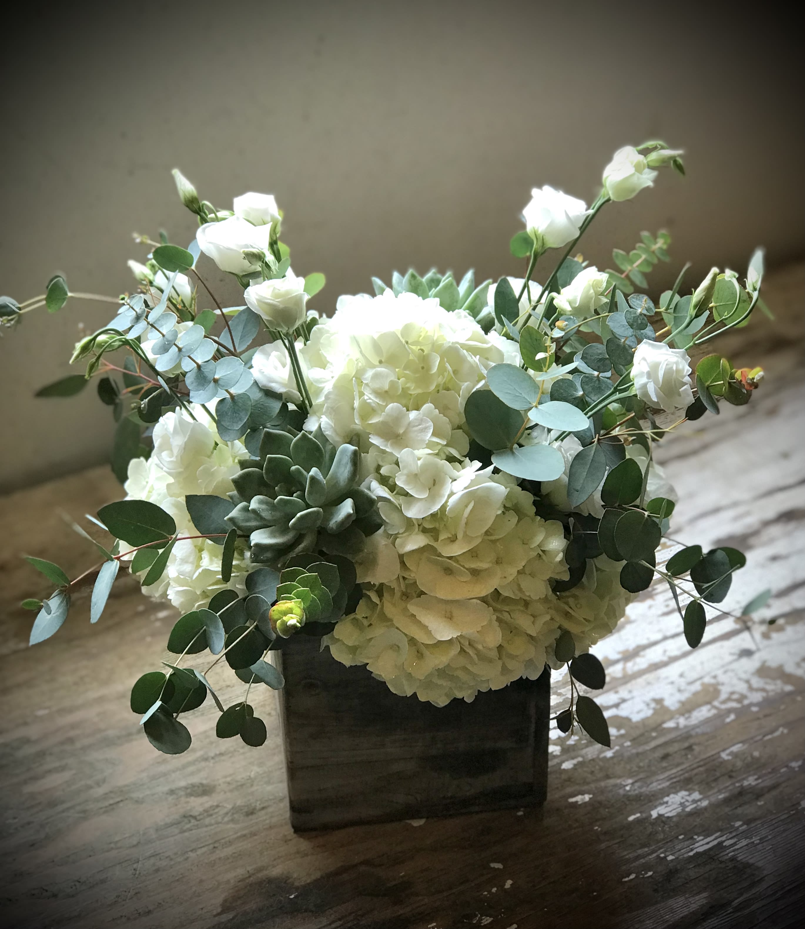 Keeping it Lite  - Cool, crisp white blooms with shades of green keep it fresh and lite! A mix unexpected textures and succulents add a unique twist that suites any style, all gathered in a square gray flower box container.