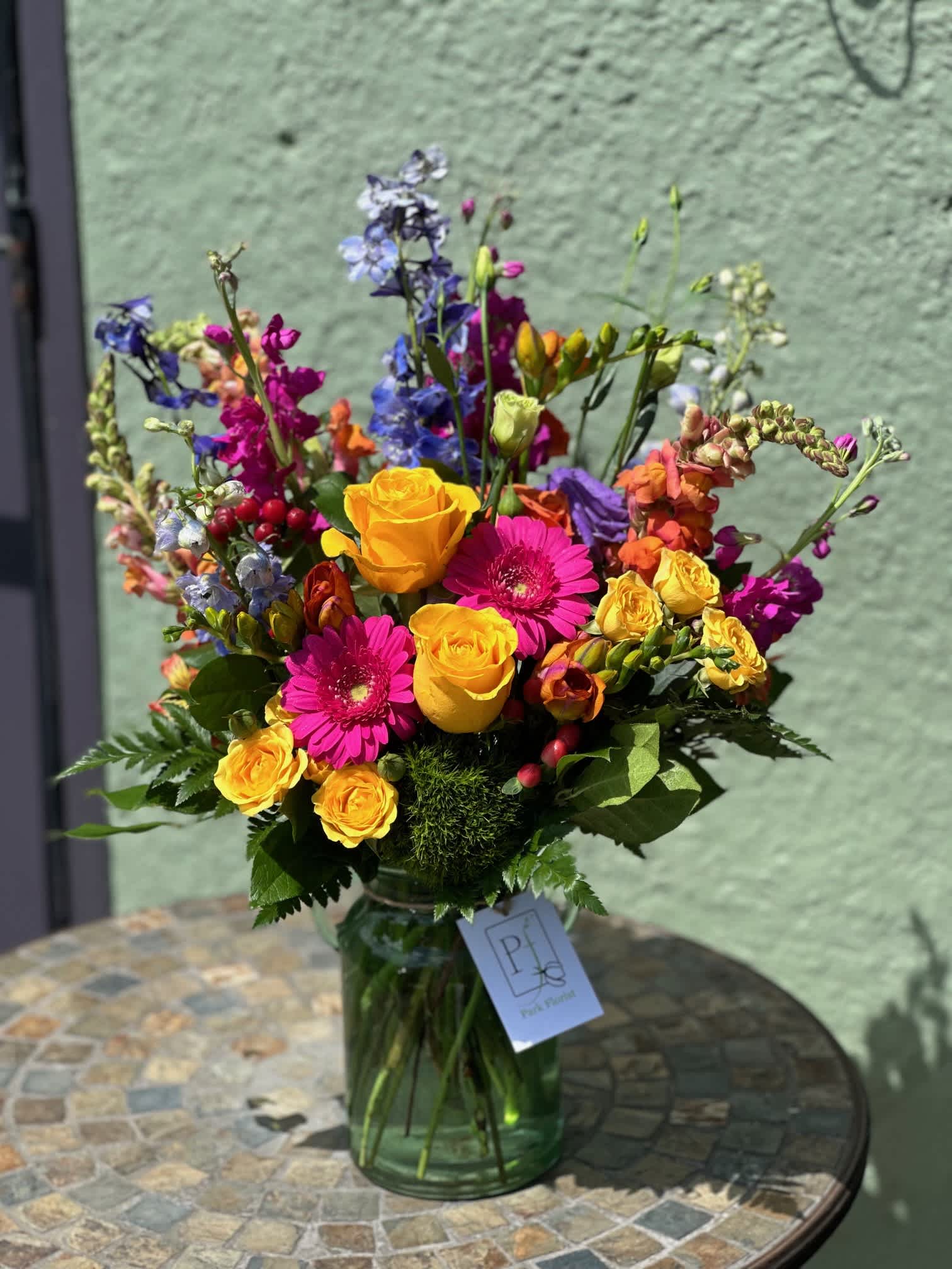 Chesapeake - Yellows and pinks are surrounded by stunning ocean blues in &quot;Chesapeake&quot; which reminds us of a warm day by the Bay. Roses, gerbera daisies, lisianthus, freesia, stock, and deliphinium help to paint a wonderful beachside view in a glass vase. 