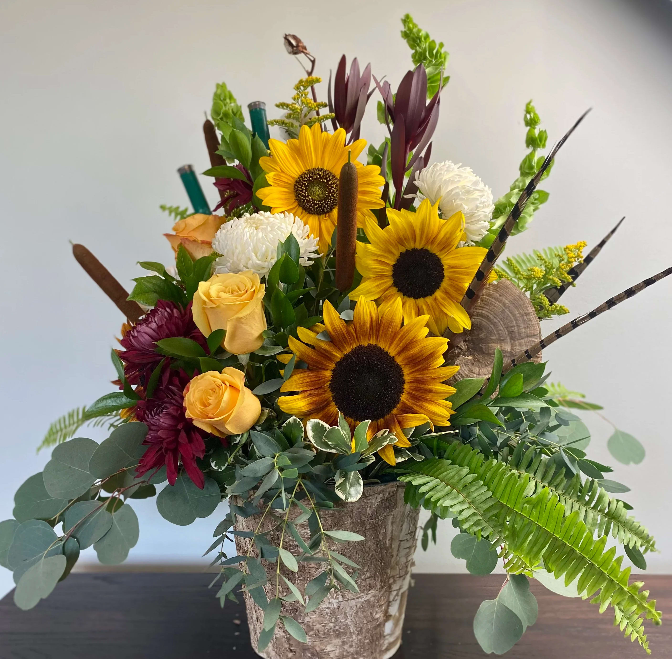 Vintage Classic Vintage Classic - A robust arrangement with touches of natural elements and rich colors. Including Sunflowers, Burgundy Chrysanthemums, White Chrysanthemums, Yellow Roses, Bells of Ireland, Solidago, Leucadendron, Cattails, Pheasant Feathers, and mixed greens in a birch bark pot.