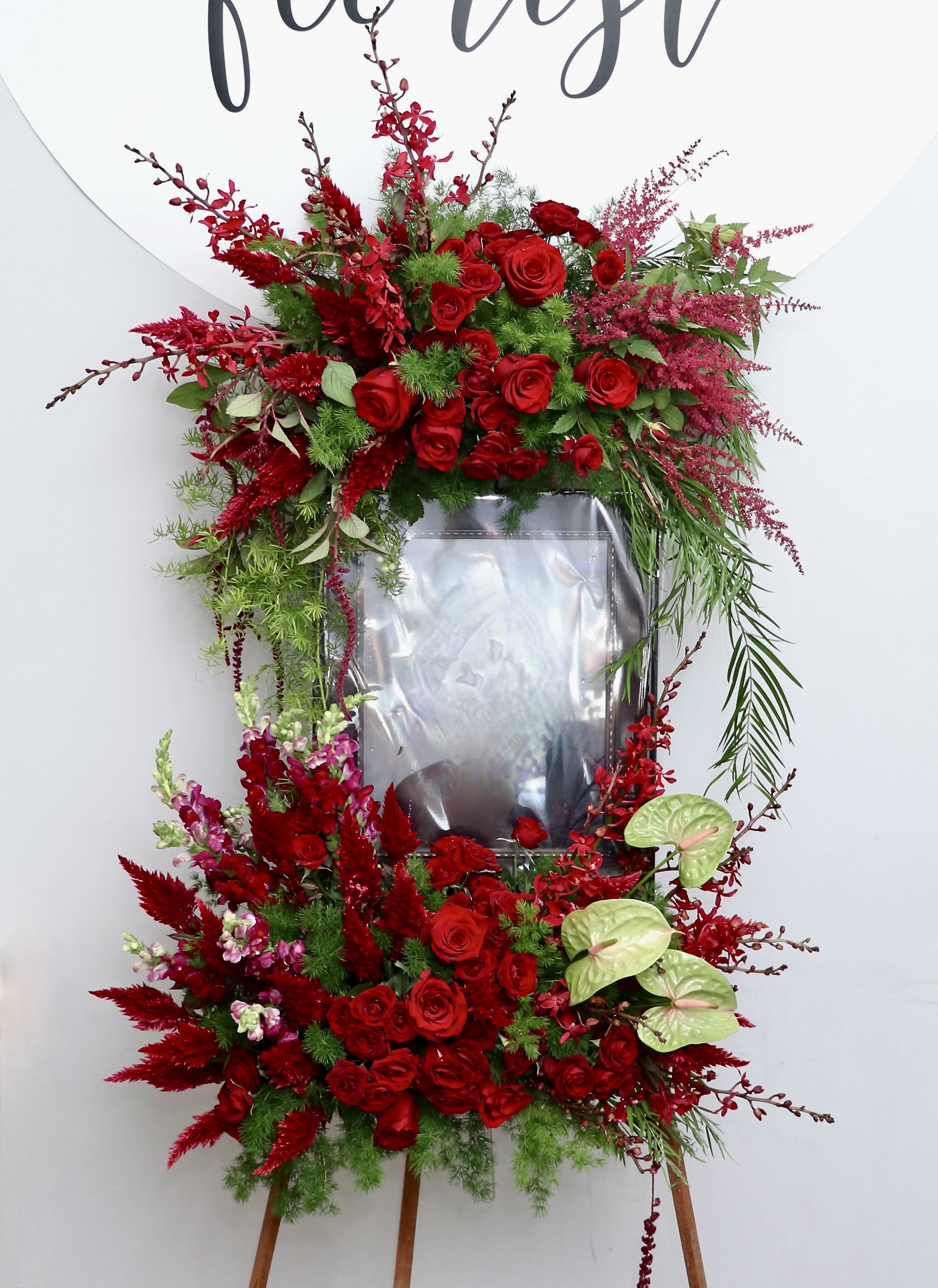Red Rembrance Frame Red Rembrance Frame - This stunning frame is made with red roses and other gorgeous red florals. It will frame your loved one beautifully as the flowers and greenery drape and curve around their portrait. 11" x 14" frame is not included, please coordinate with us for drop off. We include easel, printed banner, and delivery (some fees may apply). An additional banner can be added for $15