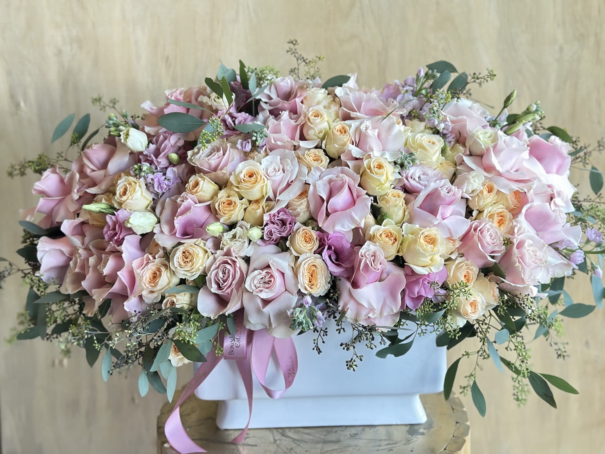 Blush Harmony Blush Harmony - A luxurious garden-style arrangement overflowing with pastel roses in shades of blush pink, peach, and cream, delicately accented with sprigs of eucalyptus and soft lavender blooms. Designed in a modern white vase and finished with satin ribbons, this elegant piece radiates romance and sophistication—perfect for weddings, anniversaries, or any occasion that calls for beauty and grace.