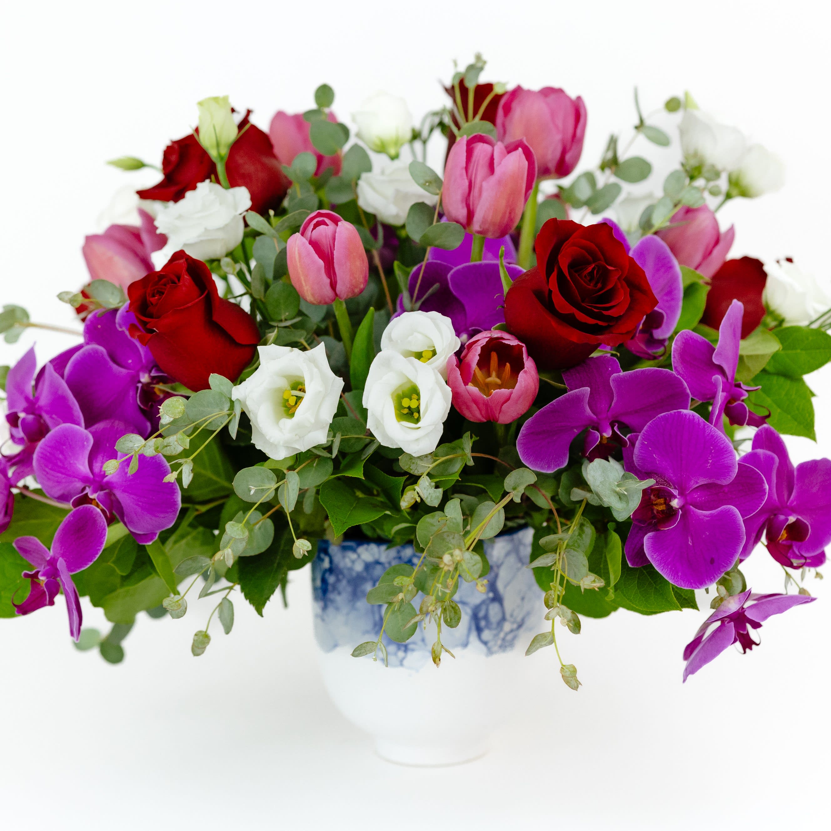 Everlasting Elegance - A beautiful arrangement of classical blossoms. Six traditional red roses have been modernized by combining with 3 gorgeous purple orchids and 10 stunning pink tulips. Eucalyptus is added to really elevate the look and a cute blue and white container allows these flowers to really shine.   FAQ  Q: What time will my flowers arrive and what if no-one is there to accept them? A: Excellent question! We’re unable to provide or guarantee specific delivery times. All our flowers are delivered anytime between 9-5pm, with exception to Sympathy designs for a funeral service. For full details around our delivery process and timings, please see our Terms and Conditions. Q: What days do you deliver flowers? A: All our flowers are available for San Francisco and Daly City delivery seven days a week, between 9am-5pm. Q: May I order for the same day delivery? A: Yes, same day deliveries are available if you place an order before 1pm. Q: May I request to change the design a bit? A: Yes, please make a note in the SPECIAL INSTRUCTION box when you place your online order. We will do our best to follow them. Q: Will my flowers look exactly as what is pictured? A: Depending on the season, colors or shades may vary. Sometimes we need to substitute flowers due to seasonal availability, but they’re always substituted for the same or greater value.  Ready to bring floral beauty into someone’s world with our romantic vase of red roses? Order this gift online now or give us a call on (415) 752-2060 if you have a question or special request.