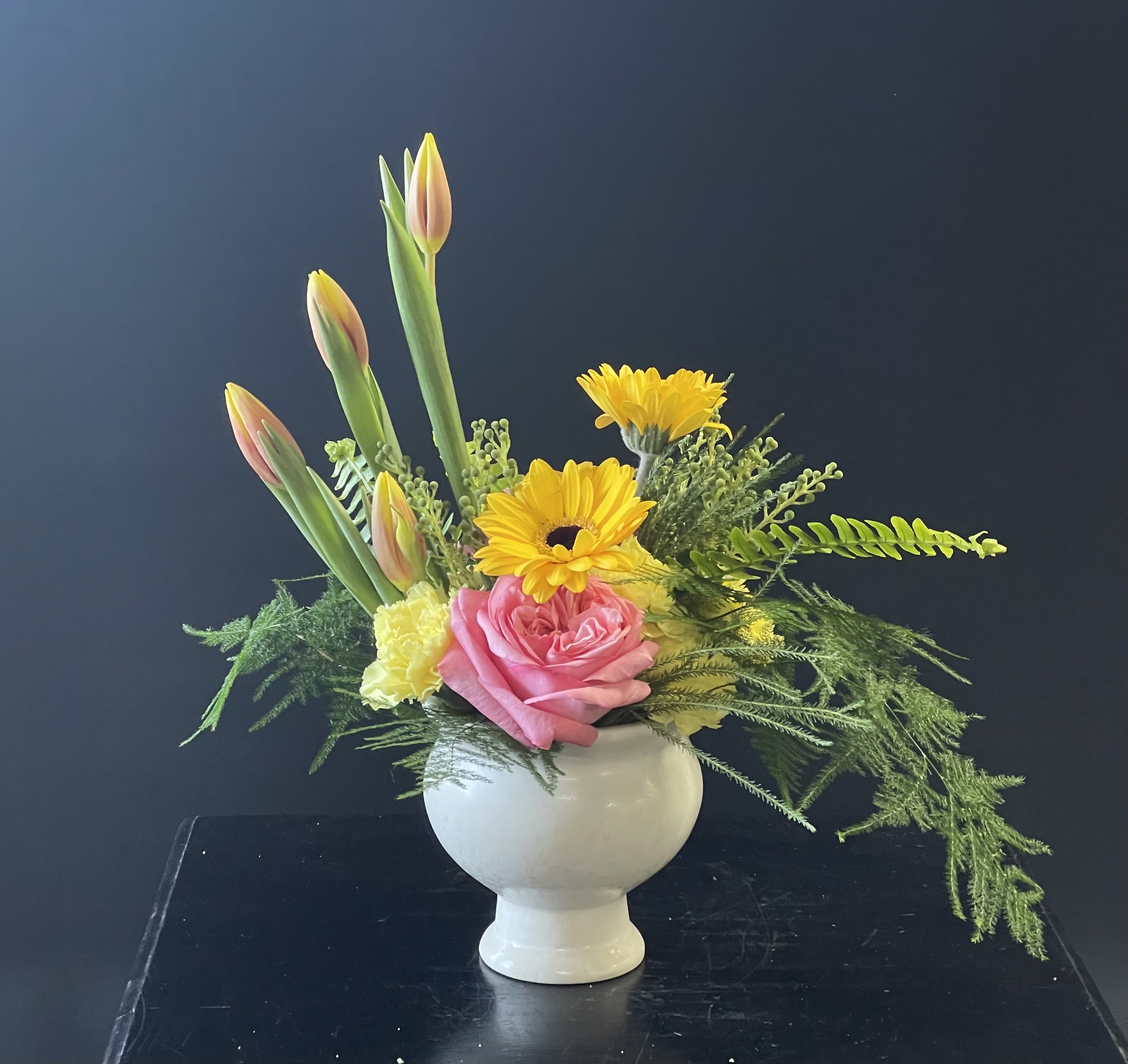 Poise Flower Arrangement  - Roses and carnations nestled under gerberas and tulips.  In a ceramic pedestal bowl.  This arrangement is very small and perfect for a desk.