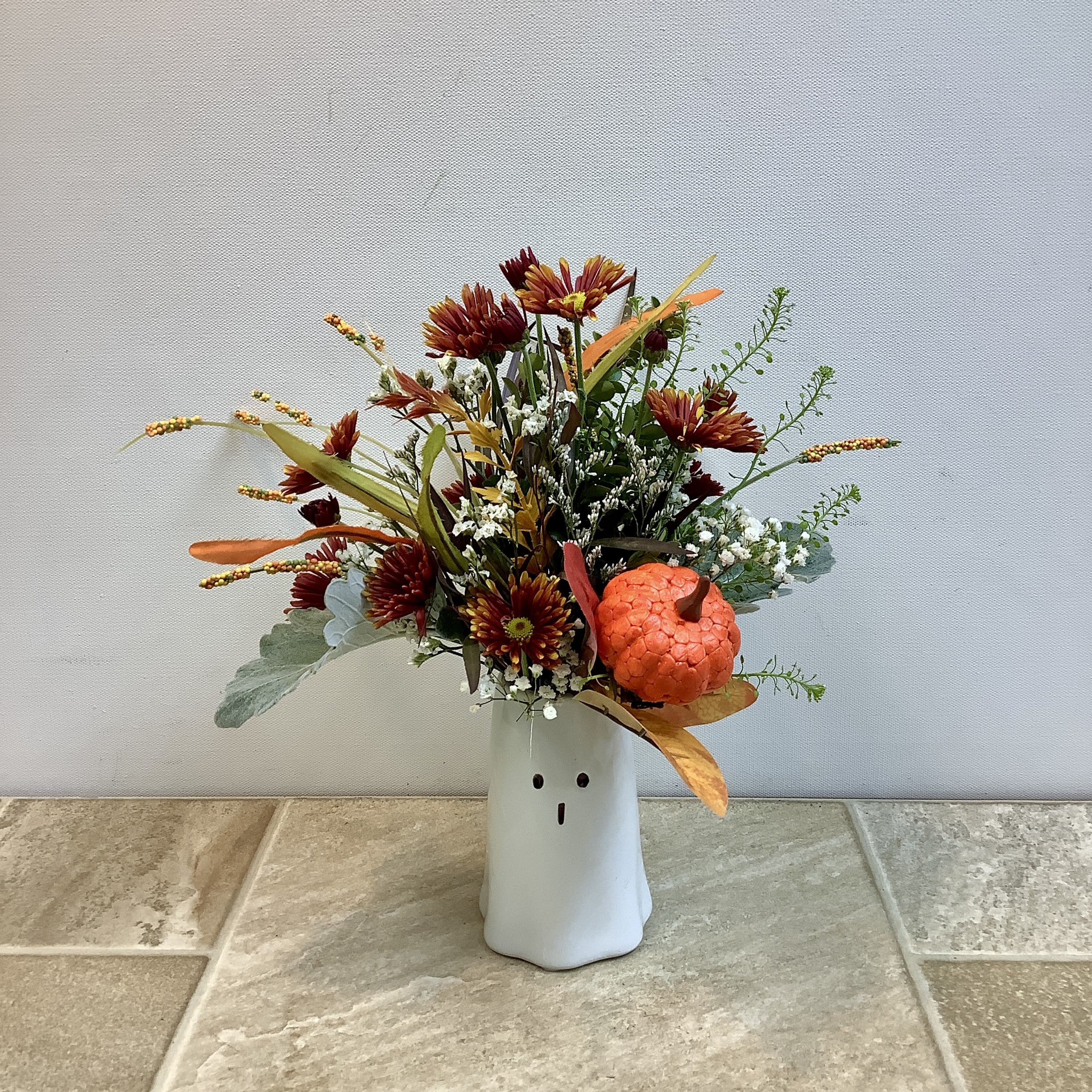 Bitty BOO-quet Bitty BOO-quet - This cute and whimsical "boo-quet" in a small white ceramic ghost vase with a "boo" expression is perfect for Halloween lovers. A rust-colored mum is joined by baby's breath, green foliage, and fall grasses. A bright orange mini pumpkin completes the festive feel. Approximate size: 10" w x 12" h. A larger "BOO-quet" arrangement is also available.