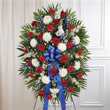 Red, White &amp; Blue Sympathy Standing Spray - They served their country with honor and pride, which is how they should be remembered. Our patriotic standing spray arrangement is meticulously handcrafted by our expert florists to honor a brave veteran who has passed away. Filled with fresh blooms in red, white and blue for a lush, full presentation, it’s a proud and fitting final tribute. •Standing spray arrangement with red roses and carnations; white football mums, gladiola and monte casino; blue delphinium; purple limonium; accented with soft, lush greenery and satin ribbon •Measures approximately 46&quot;H x 34&quot;L without stand •Arrives on an easel •Appropriate for the funeral home or gravesite •Our florists hand-design each arrangement, so colors and varieties may vary due to local availability
