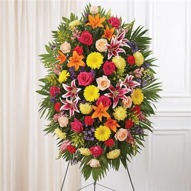 Bright Sympathy Standing Spray - Their passion and joy for life will always be remembered. Our impressive standing spray arrangement was designed to capture that colorful spirit. Meticulously handcrafted by expert local florists for a lush, full presentation, this vibrant mix of blooms creates a grand and memorable tribute. •Standing spray arrangement with red carnations; orange Asiatic lilies; yellow Gerbera daisies and football mums; peach and hot pink roses; pink snapdragons; purple statice and monte casino; accented with soft, lush greenery •Large measures approximately 56&quot;H x 38&quot;L without stand •Medium measures approximately 46&quot;H x 34&quot;L without stand •Small measures approximately 42&quot;H x 30&quot;L without stand •Arrives on an easel •Appropriate for the funeral home or gravesite •Our florists use only the freshest flowers available, so colors and varieties may vary due to local availability