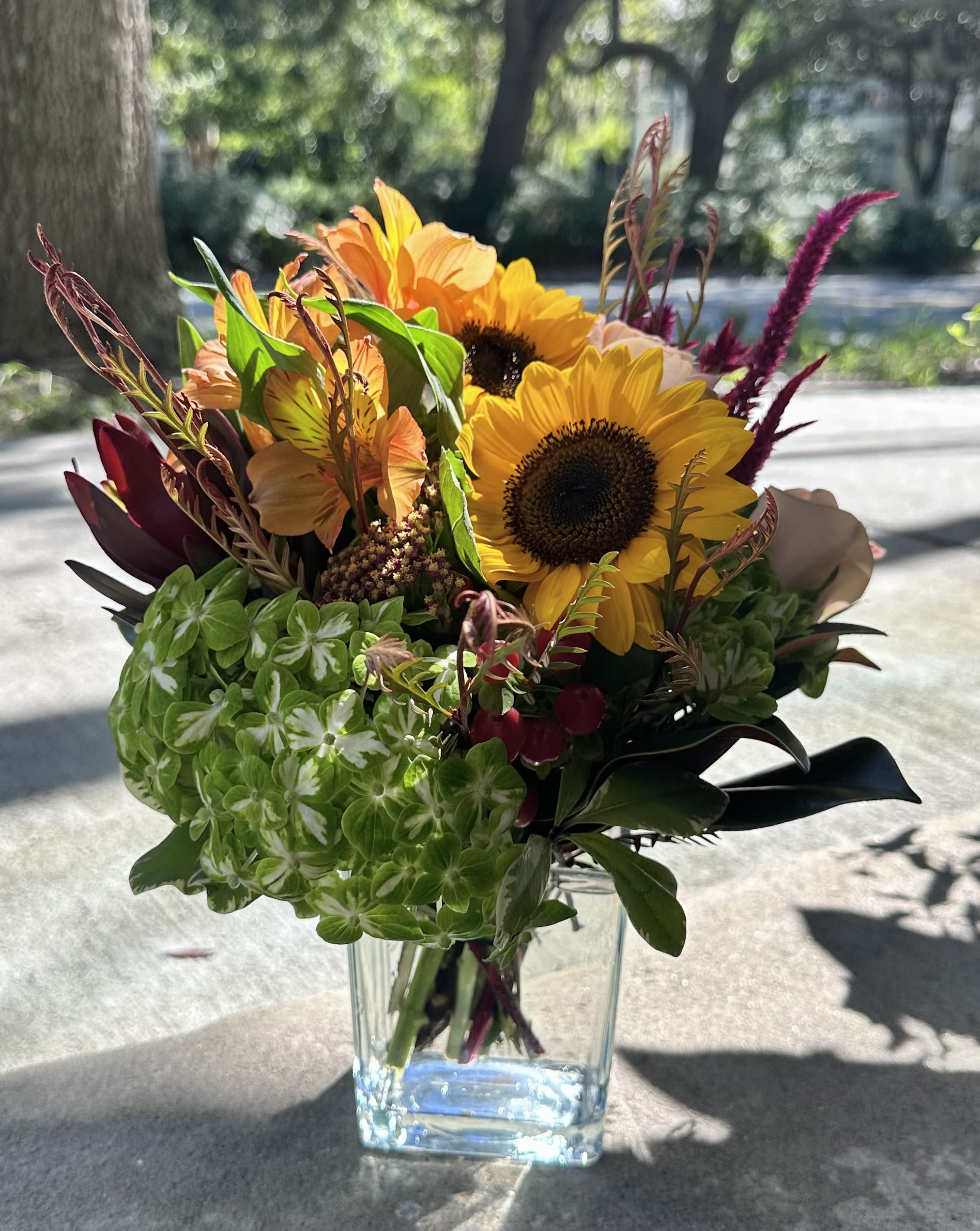 Mae's Fall Garden Mae's Fall Garden - ( Pictured as a Deluxe) The Fall Version of a Flower Cottage favorite. This arrangement bursts with the rich, warm tones of autumn—sunlit golds, deep oranges, rustic reds, and earthy greens blending together for a cozy, seasonal look. The mix of textures and heights gives it a natural, gathered-from-the-garden feel, while the clear glass vase adds a touch of modern simplicity. Perfect for bringing the warmth and vibrance of fall indoors.