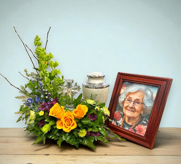 Heavenly Garden Urn & Photo Tribute Heavenly Garden Urn & Photo Tribute - The Heavenly Garden Urn and Photo Tribute showcases a peaceful and meaningful display of fresh flowers, including bright yellow roses, purple chrysanthemums, and lush green foliage, accented by a keepsake glass cross. Delicate branches and sprigs of lavender enhance the arrangement, creating a calm and respectful tribute. Designed to be placed beside the urn and the framed photograph of the deceased, it adds a personal touch to honor their memory. Overall, the arrangement conveys compassion, reverence, and heartfelt remembrance.