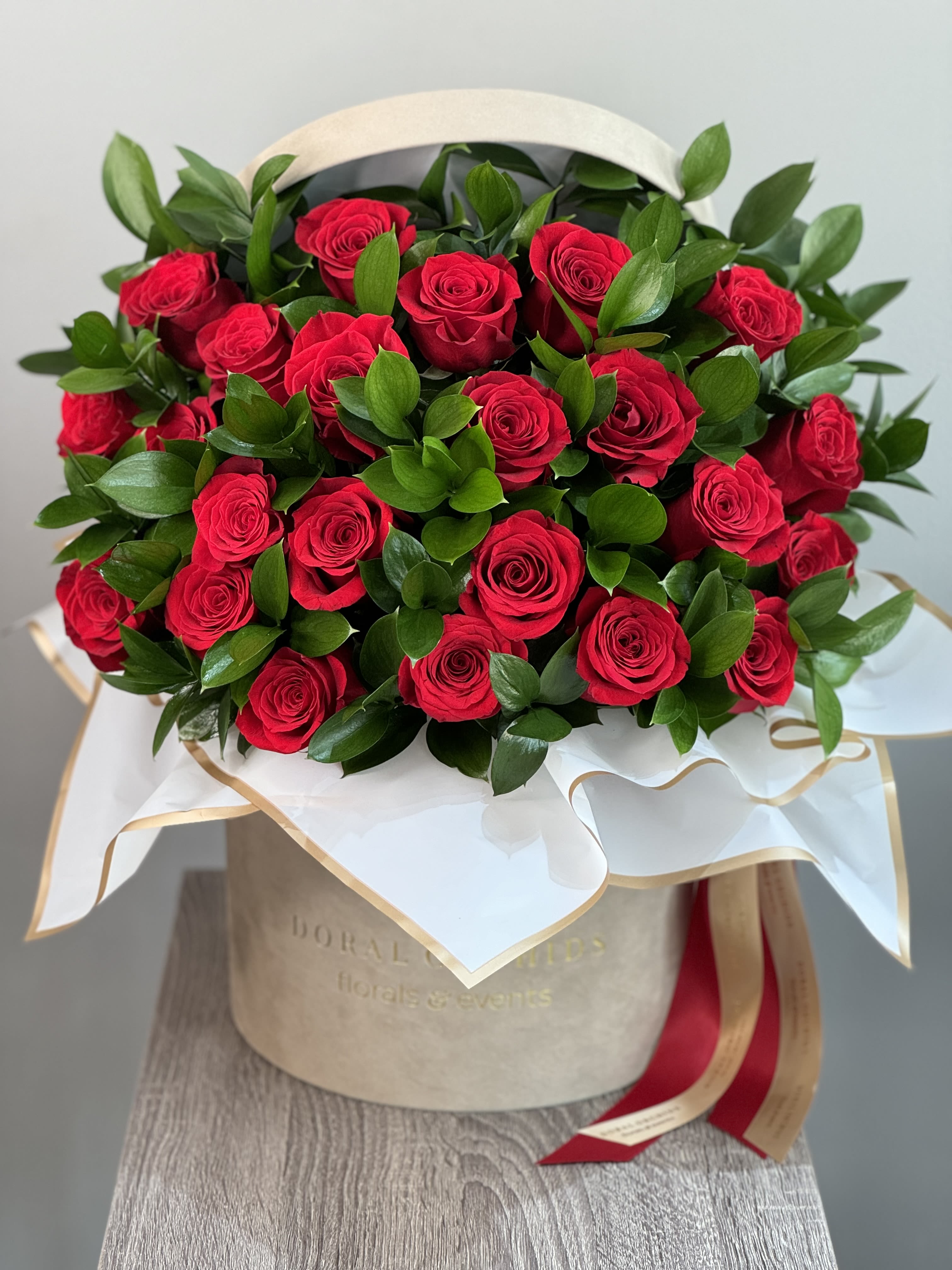 Amore in XL ™ Amore in XL ™ - A lush hatbox overflowing with vibrant red roses and fresh greenery. Wrapped in elegant white fabric and finished with a red-and-gold ribbon, this arrangement radiates timeless romance and grandeur.