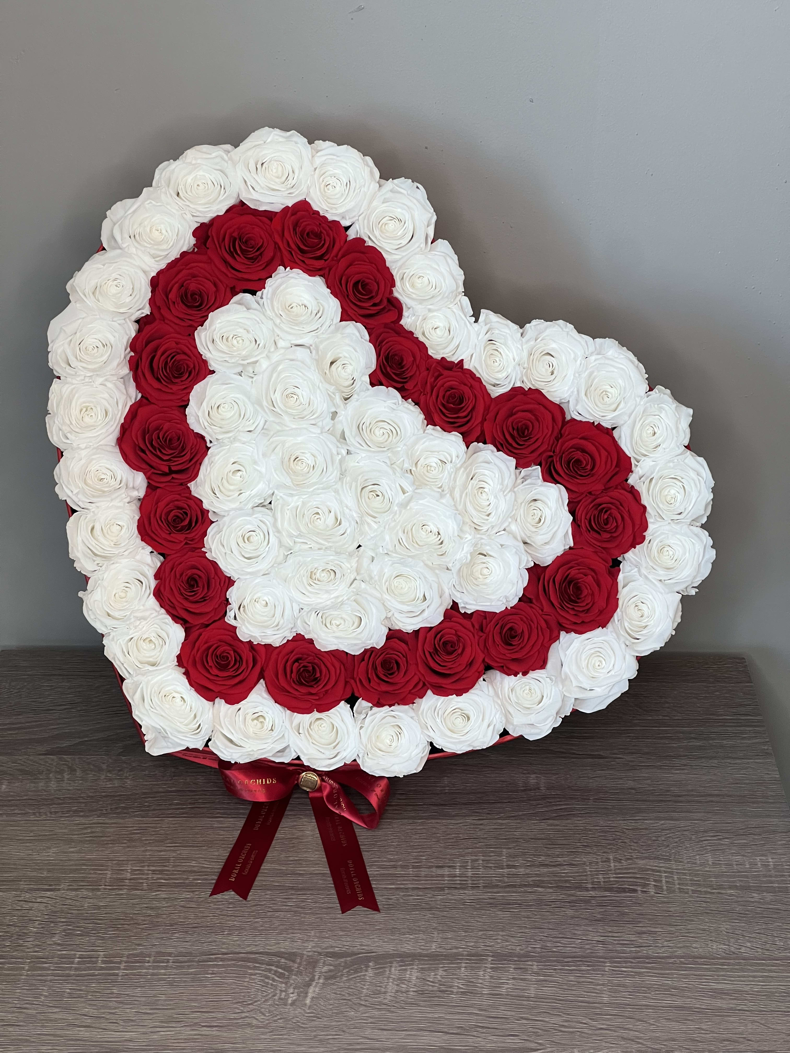Love In XL ™ - This breathtaking heart-shaped preserved arrangement features a striking pattern of white roses bordered with deep red blooms. Each natural rose is preserved to last 3 or more years, making it a timeless symbol of love and devotion. Finished with a rich red bow, it’s the ultimate statement piece for anniversaries, proposals, or any romantic celebration.