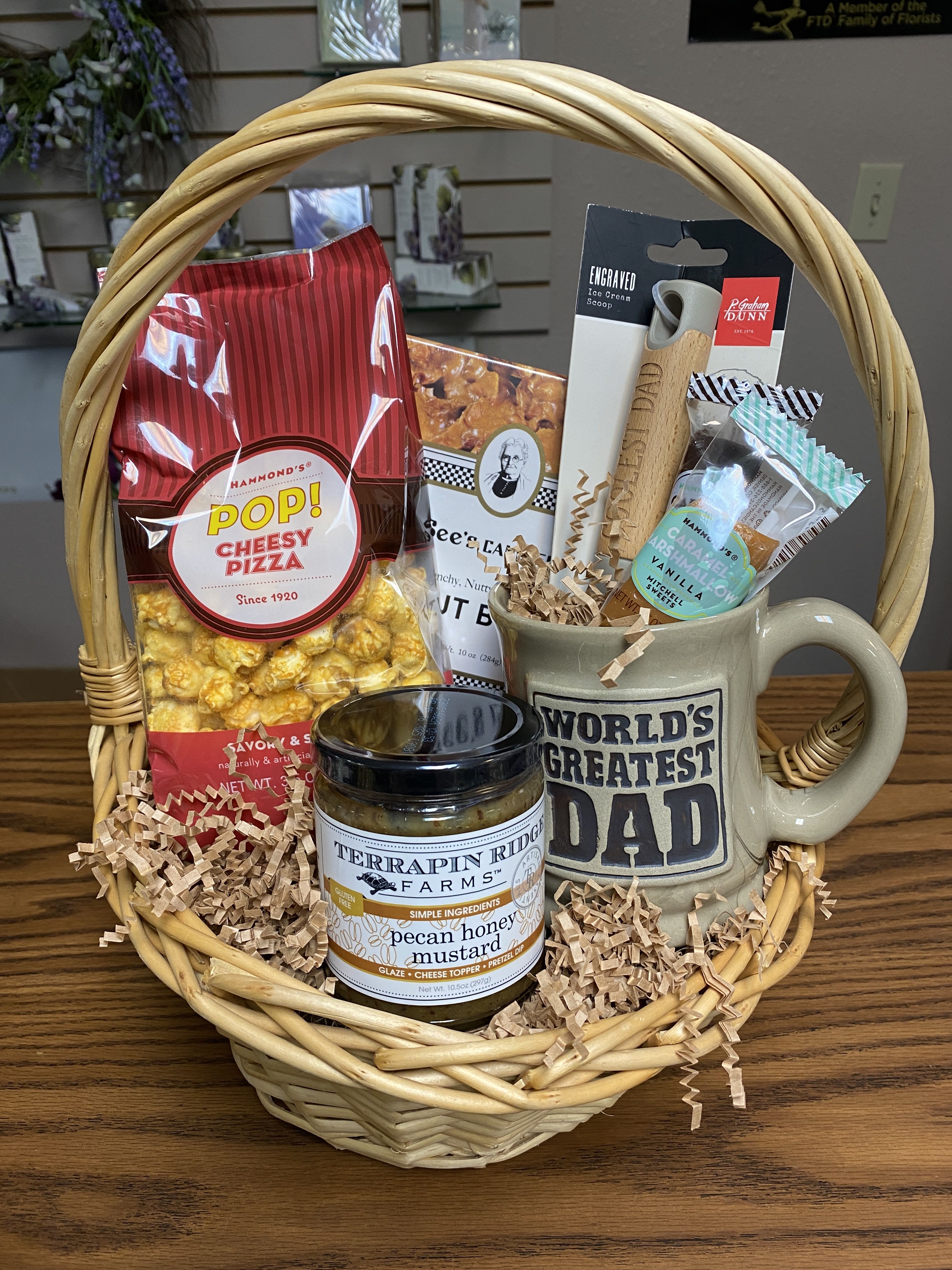 Greatest Dad Basket Greatest Dad Basket - Make a Grand Gesture this Father's Day with The Greatest Dad Basket! The basket includes: 1 Hammond's Cheesy Pizza Popcorn, 1 Pecan Honey Mustard Spread, 1 World's Greatest Dad Mug, 1 Coolest Dad Ice Cream Scoop, 1 10oz See's Peanut Brittle, and 1 Vanilla Caramel Marshmallow arranged in a basket