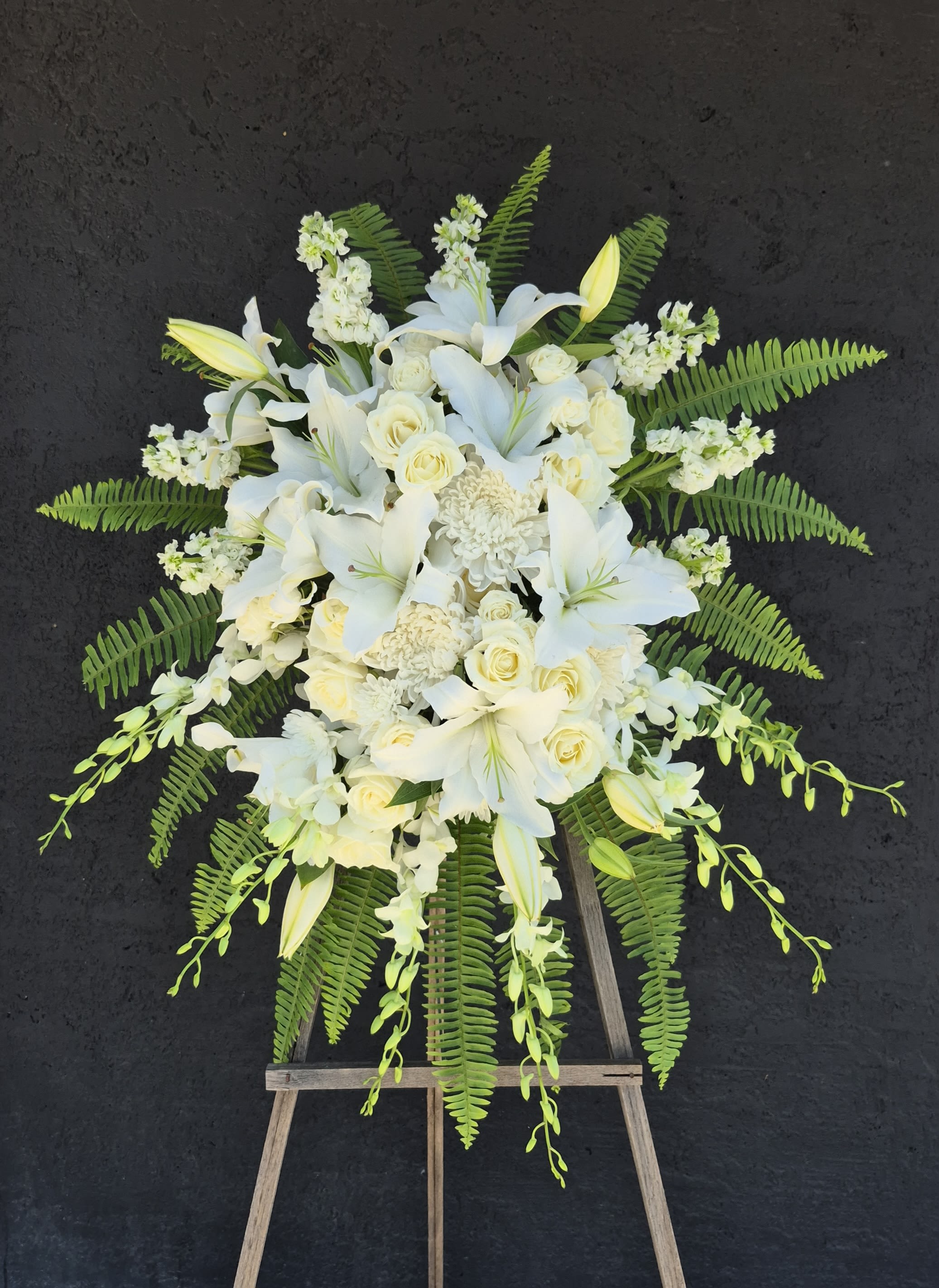 The Prayer Sympathy Standing Spray - An all white tribute, this funeral spray is pure and tranquil. Featuring a variety of white flowers and green palms this elegant funeral spray brings a feeling of peace to it's surroundings.