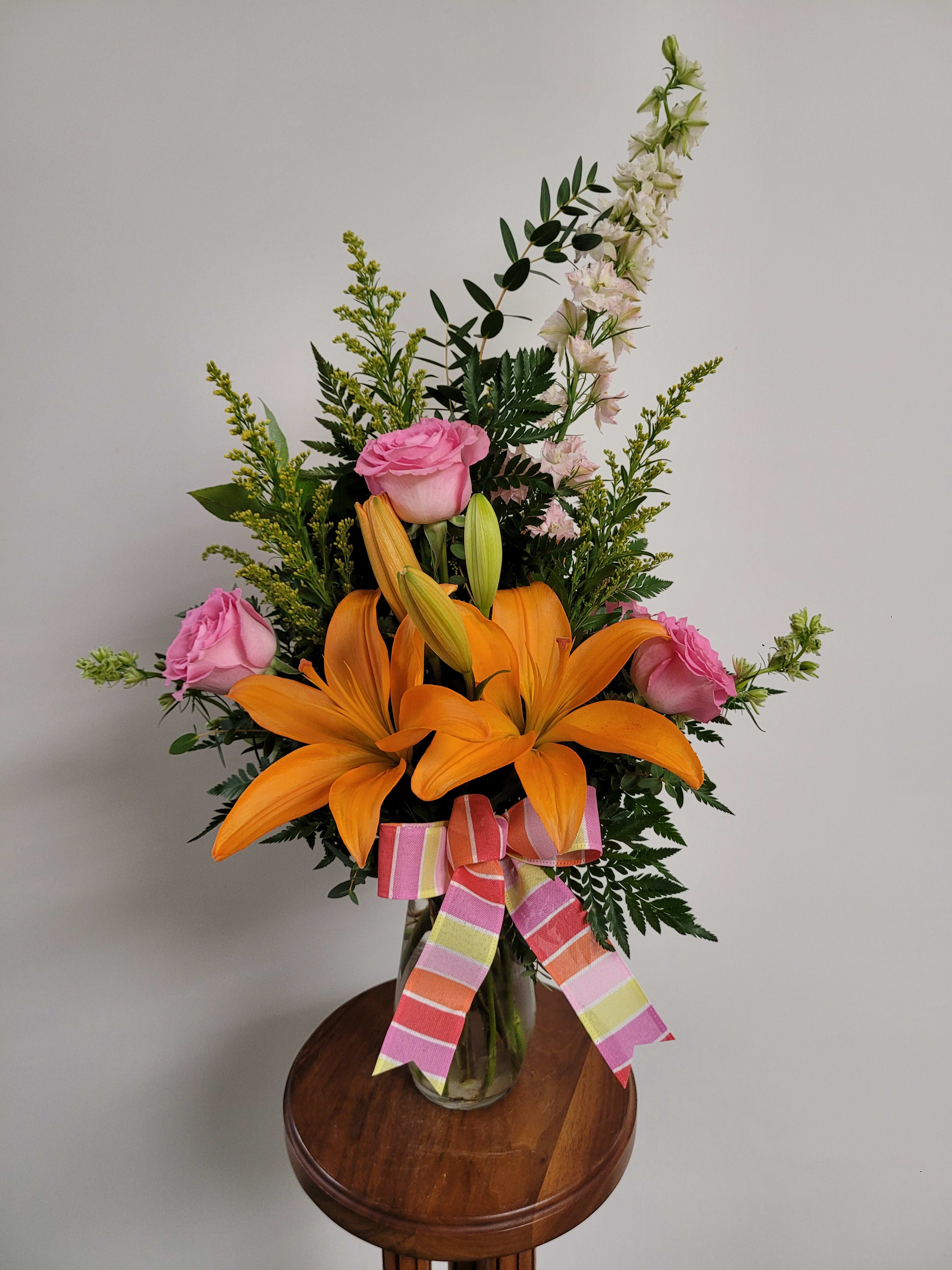 Autumn's Embrace - A perfectly sweet gesture that hints at fall while still feeling romantic. This bouquet features orange flowers and pink roses with specialty fillers and greenery. Flowers may vary due to availability. 