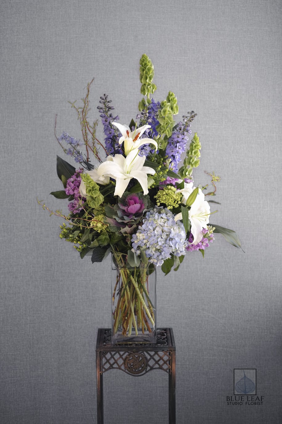Delphinium Day Dream - Beautiful, large vase arrangement of delphinium, white lilies, bells of Ireland, and an assortment of lavender flowers.(Premium upgrades to an all-around arrangement)