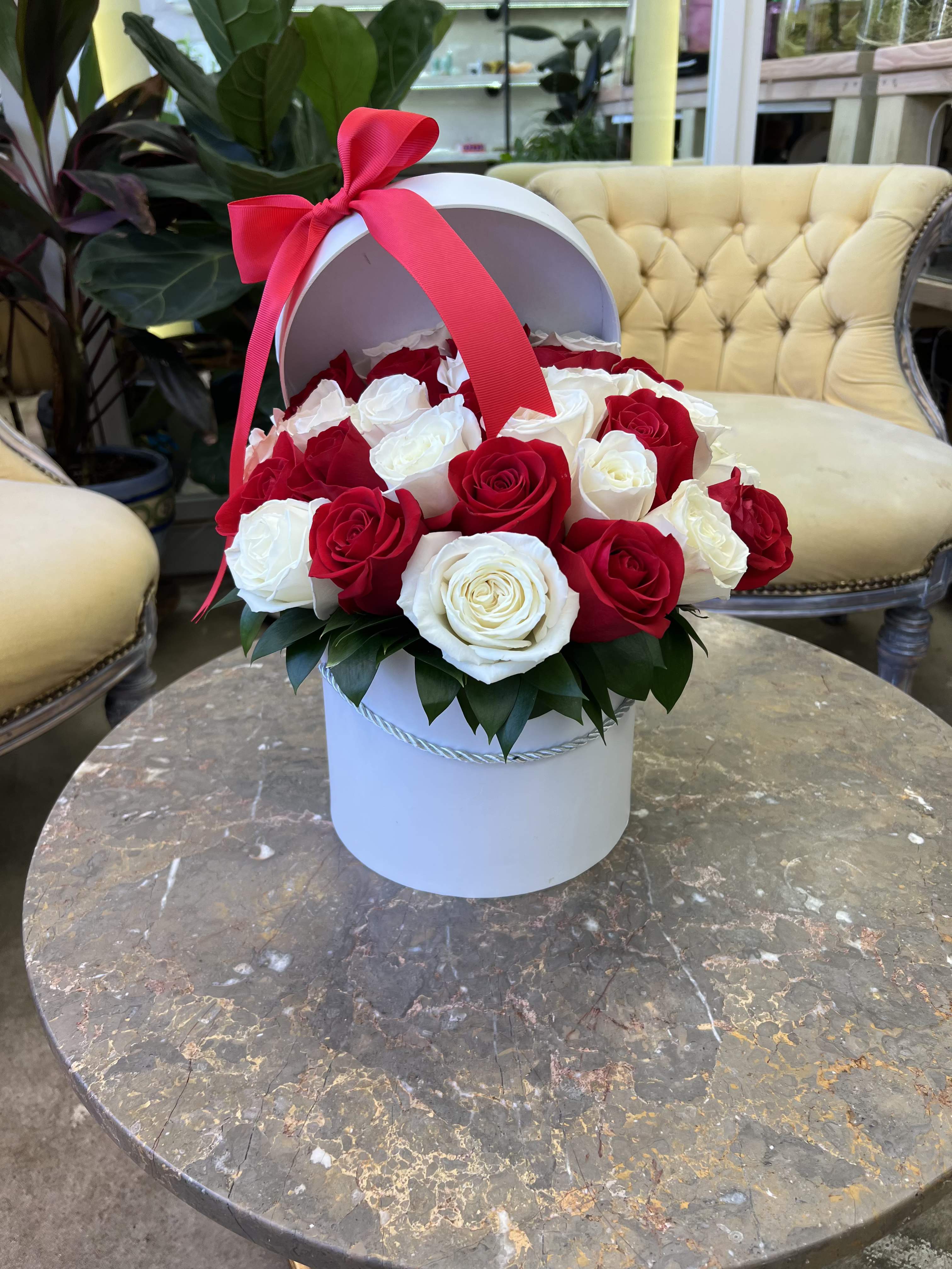 Classic Elegance - A luxurious round hat box overflowing with fresh, hand-selected roses in timeless red and creamy white. Finished with a bold satin bow, this arrangement is perfect for celebrating love, anniversaries, or making any occasion unforgettable. 