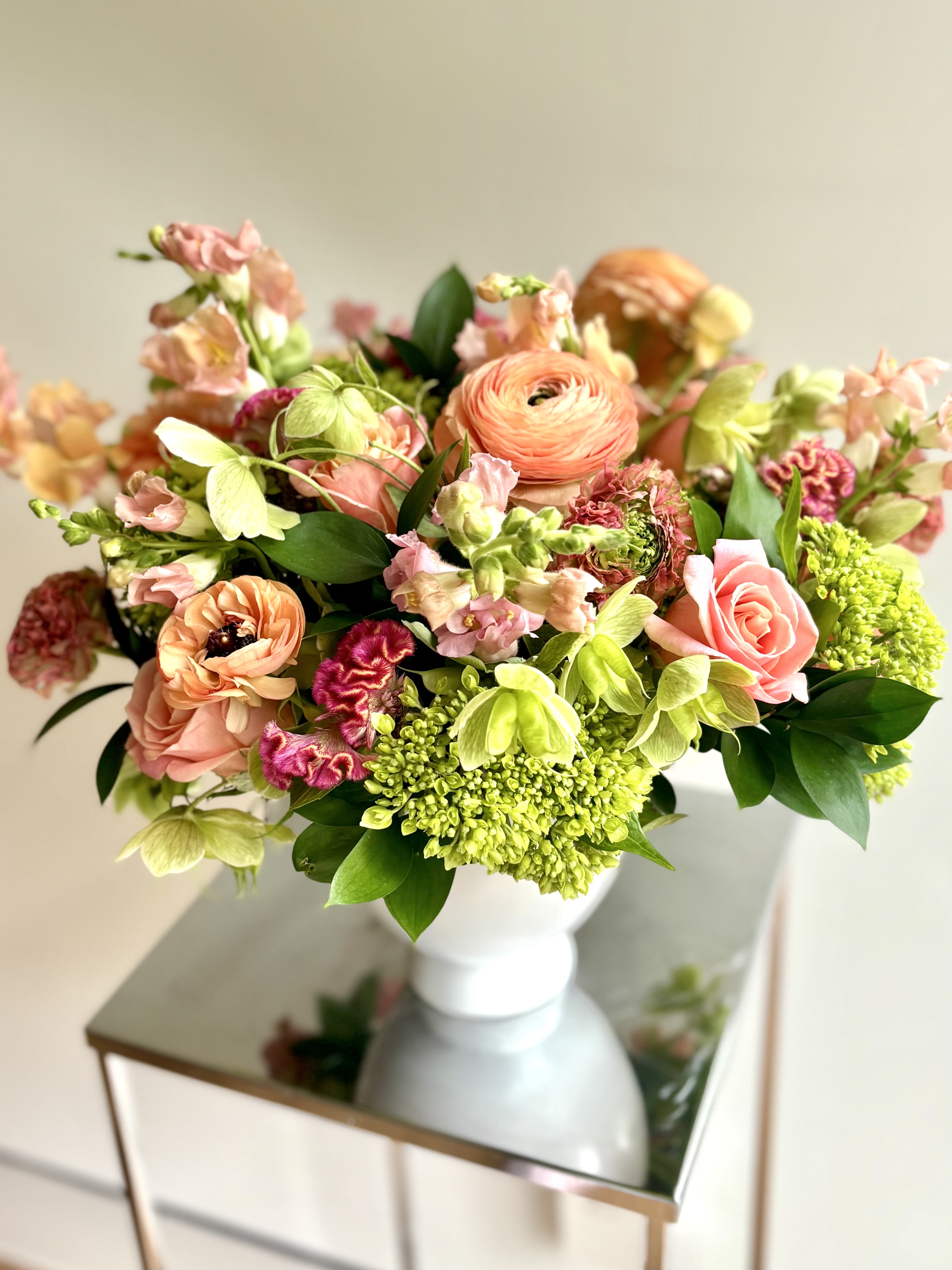 Summer Bliss Summer Bliss - A gorgeous flower arrangement in a ceramic white compote vase, filled with premium flowers in the peachy-orangey and pink color palette, nestled in green hydrangeas and ruscus foliage. The focal flowers are roses, ranunculus, and snapdragons.