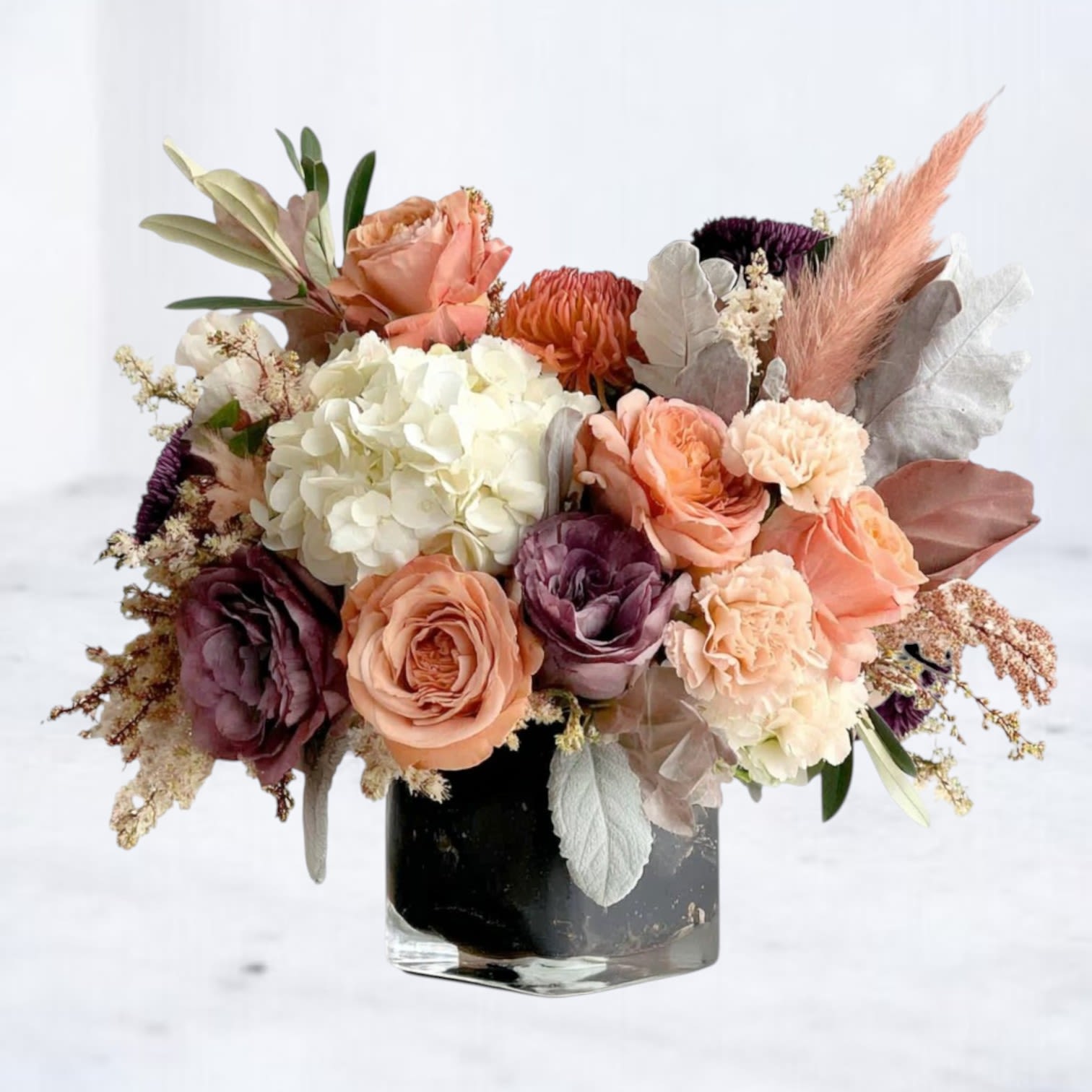Autumn Whisper Bloom - The Autumn Whisper Bloom is a refined floral arrangement that captures the warmth of fall with a touch of elegance. Featuring peach garden roses, ivory hydrangea, mauve blooms, and delicate blush spray roses, this bouquet is accented with soft dusty miller, pampas grass, and seasonal textures for a graceful finish. Arranged in a modern glass vase, it’s perfect for Thanksgiving centerpieces, fall weddings, or a thoughtful seasonal gift. Available for same-day flower delivery in Houston and surrounding areas, this autumn-inspired bouquet brings cozy sophistication to any space.